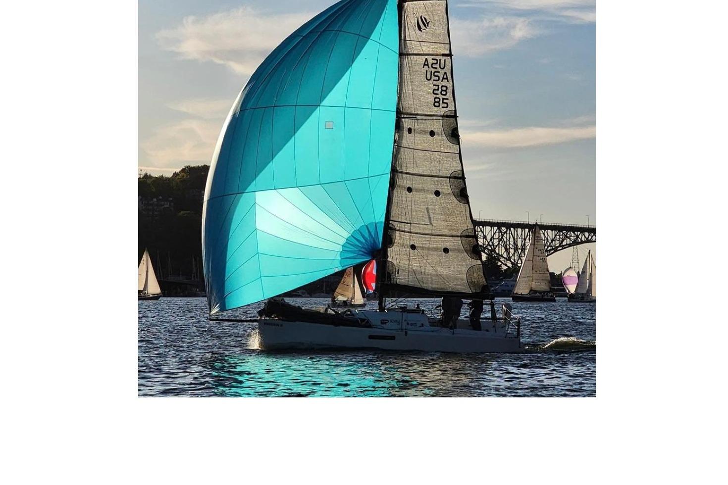 Sailboat Seascape 27 with blue spinnaker sailing near a bridge at sunset, 2018 model.
