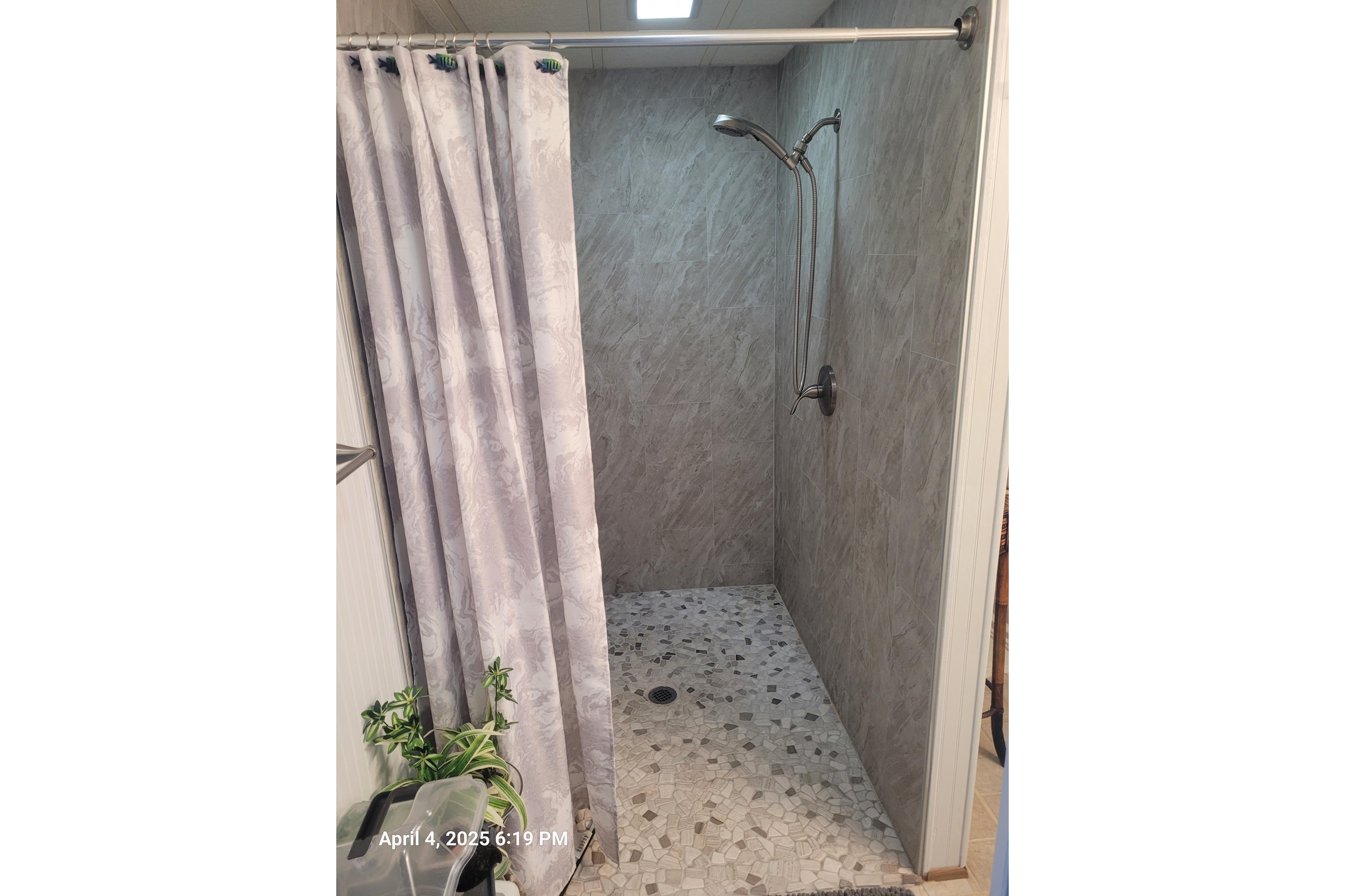 Shower area with gray tiles and curtain, plants in the foreground.