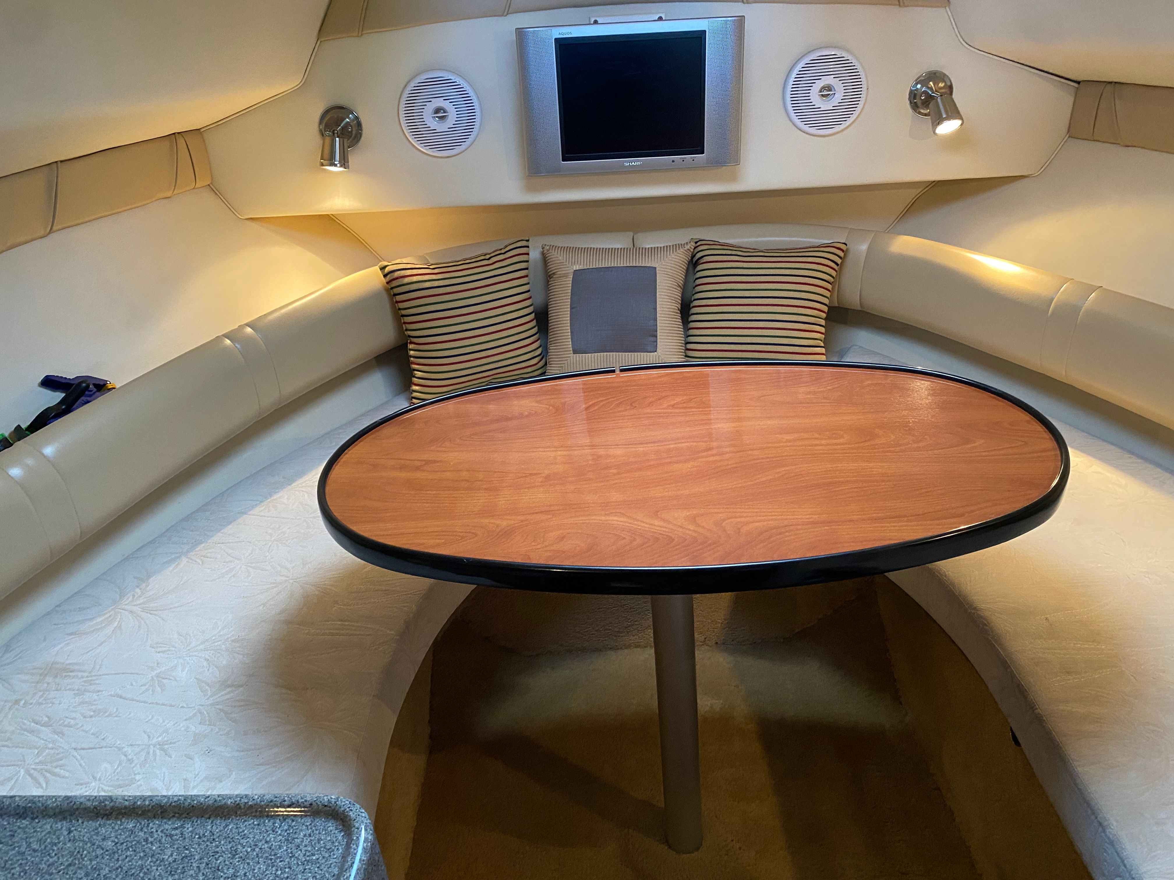 Interior of a 2005 Larson Cabrio 240 with an oval wooden table and cushioned seating.