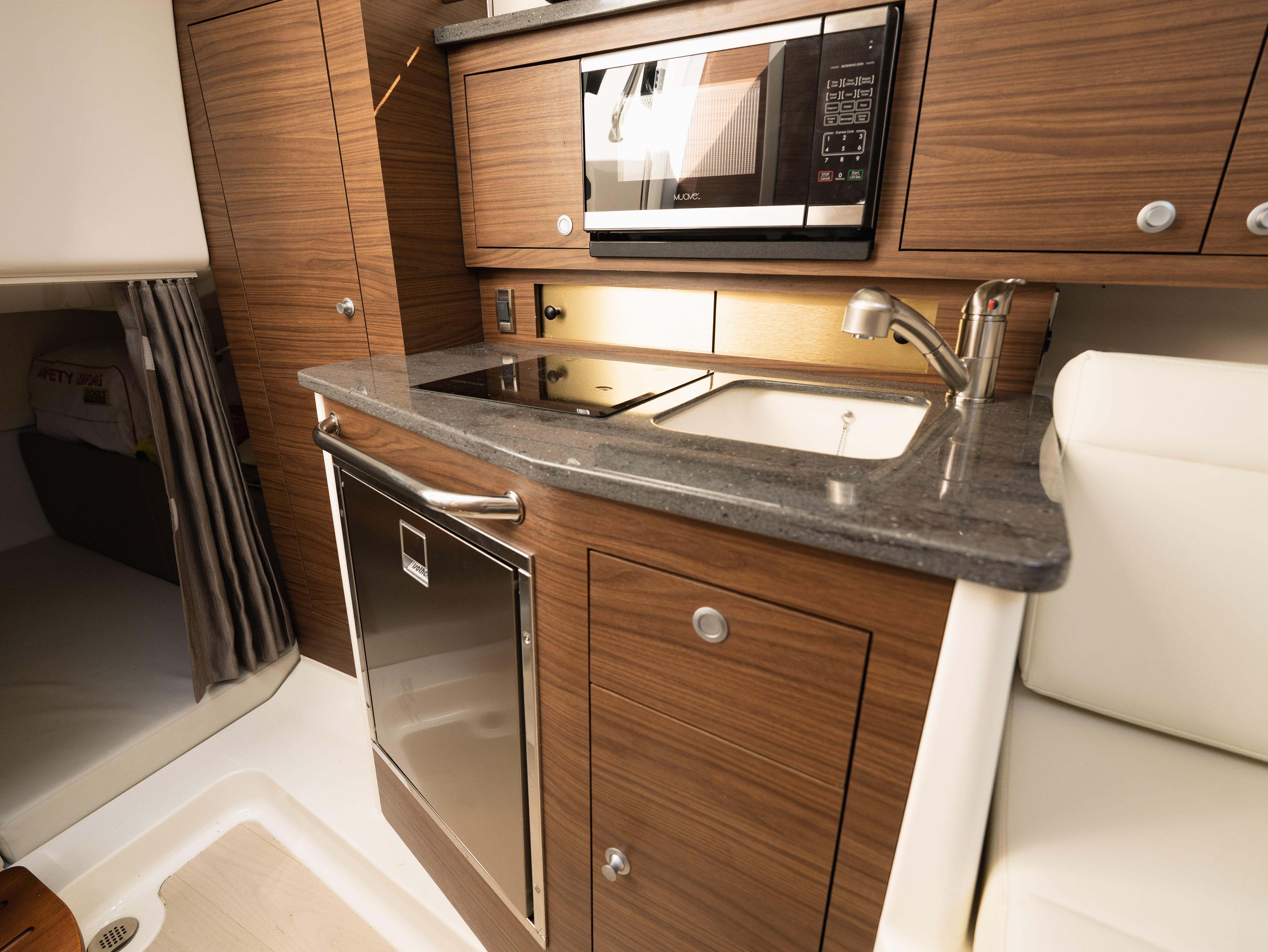 2020 Boston Whaler 325 Conquest Pilothouse kitchen with modern appliances and wood cabinetry.