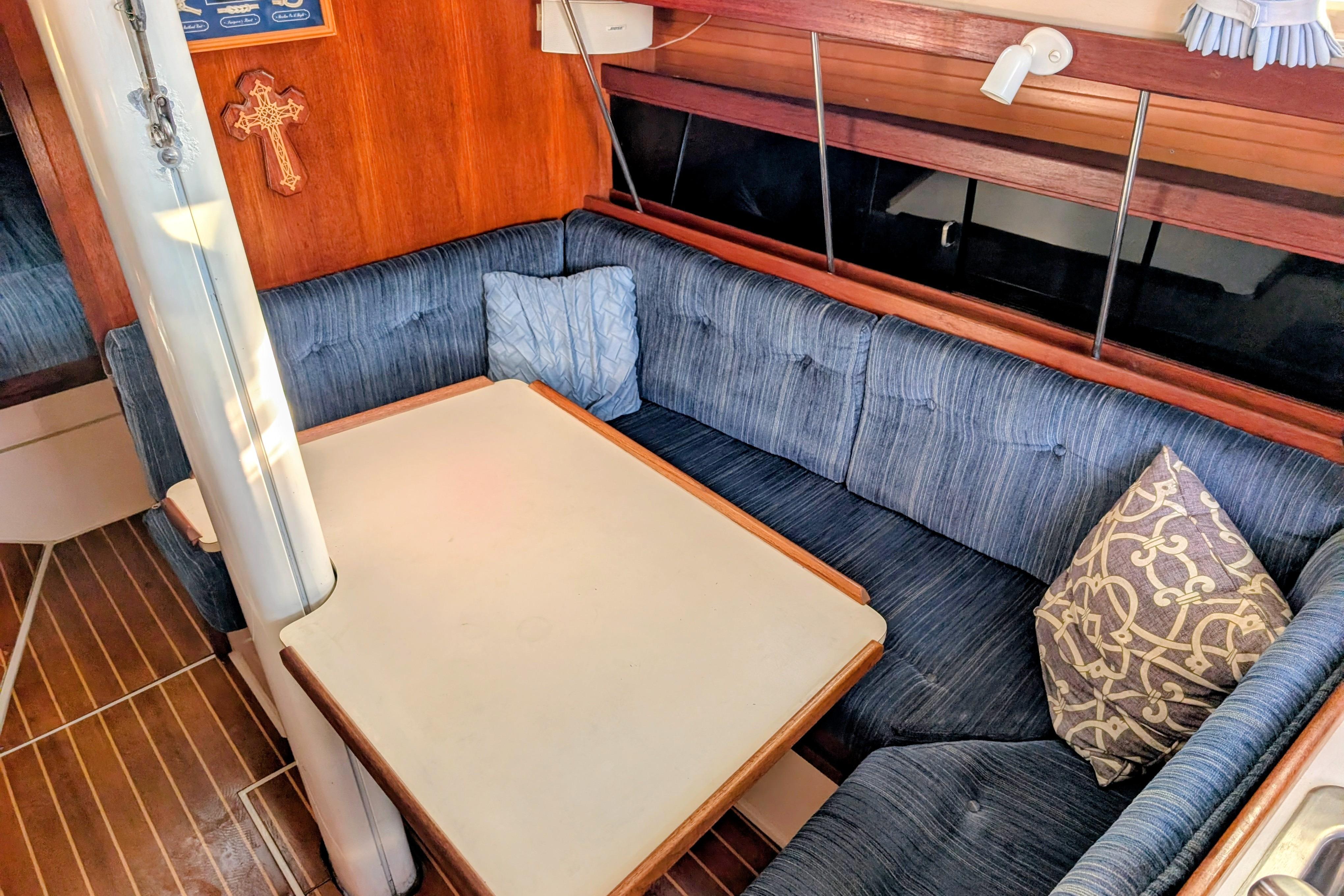 Cozy interior of a 1989 Catalina 34 sailboat with blue cushioned seating and a wooden table.