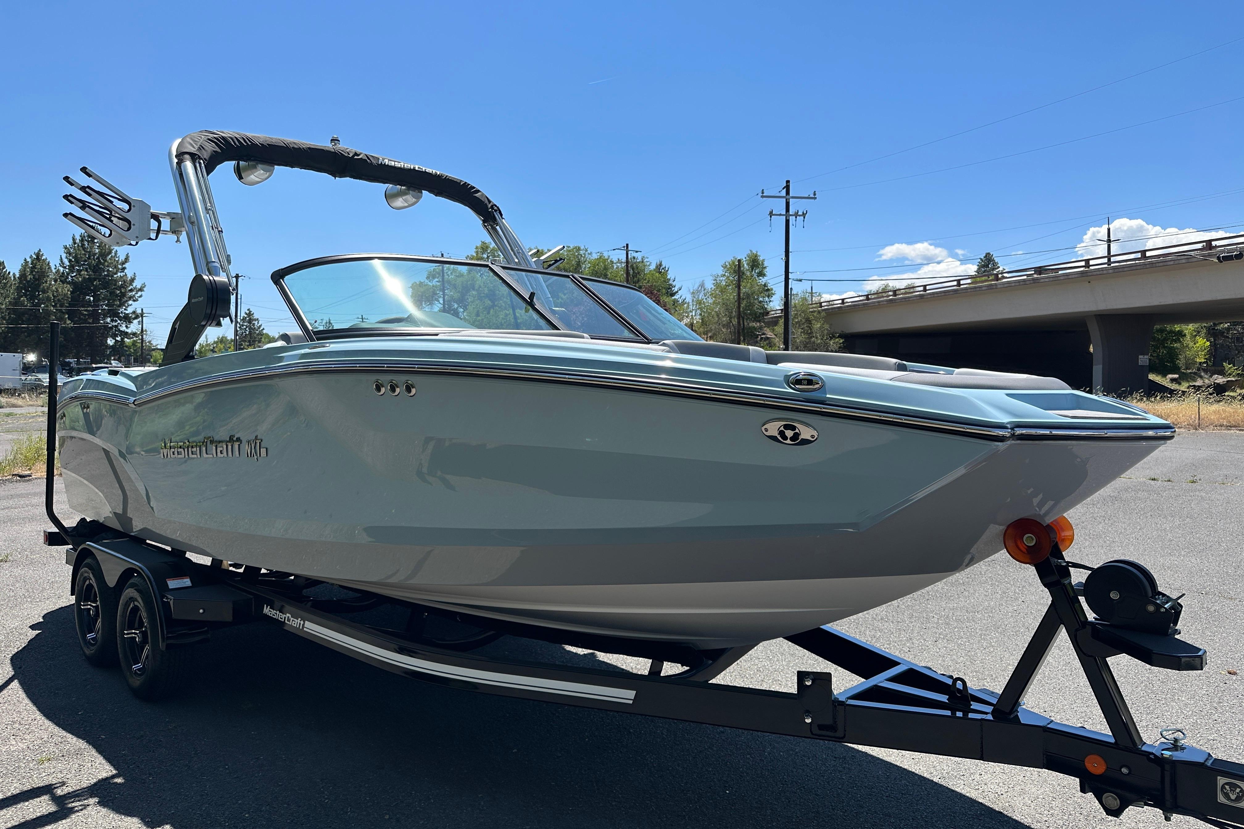 2023 MasterCraft NXT23 boat on trailer, parked outdoors under clear blue sky.