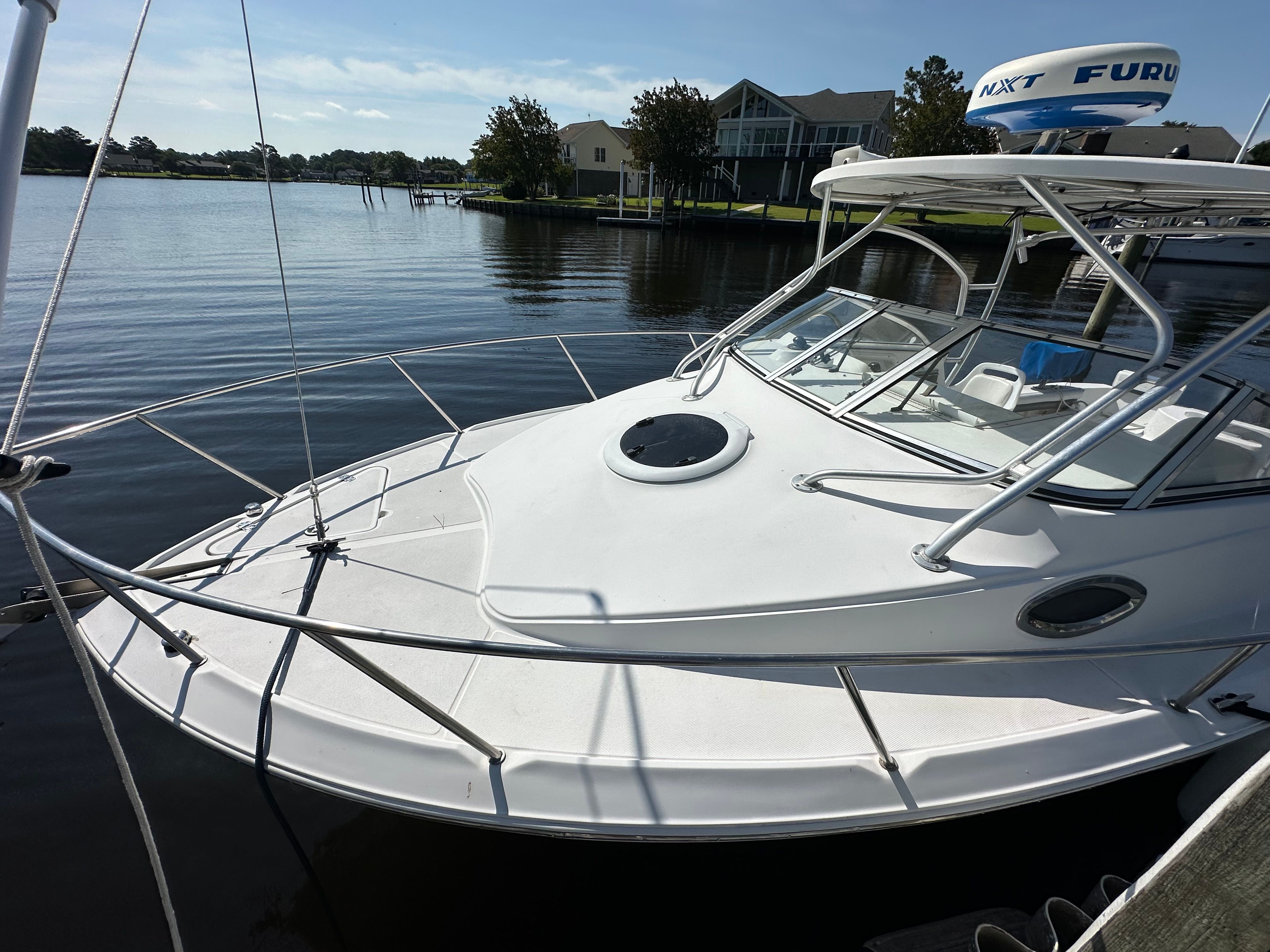 A white boat, Sea Fox 256WA, docked on calm water with houses in the background.