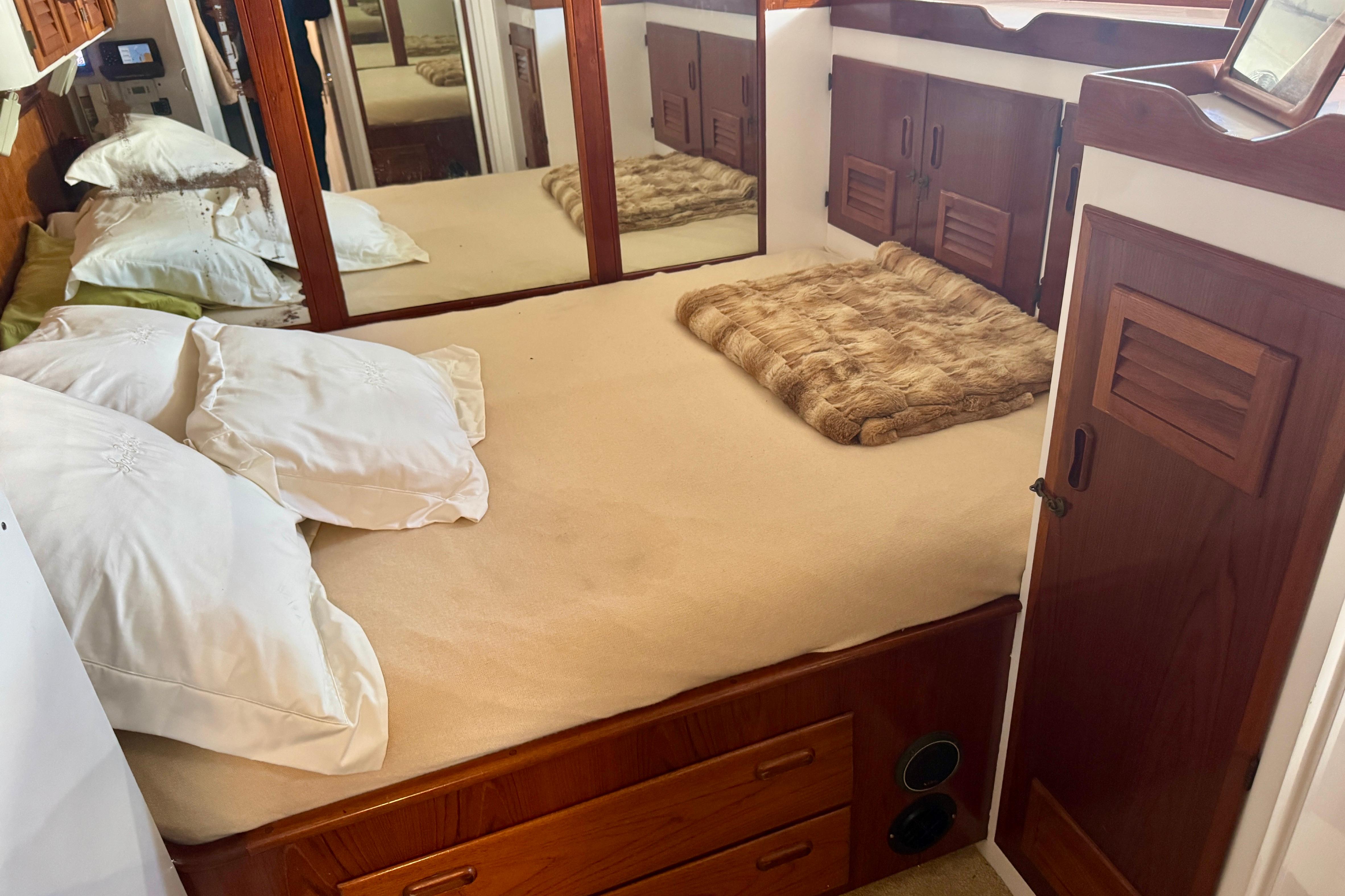 Cozy bedroom in a 1958 Blanchard Pilothouse boat with wooden cabinetry and mirrored walls.