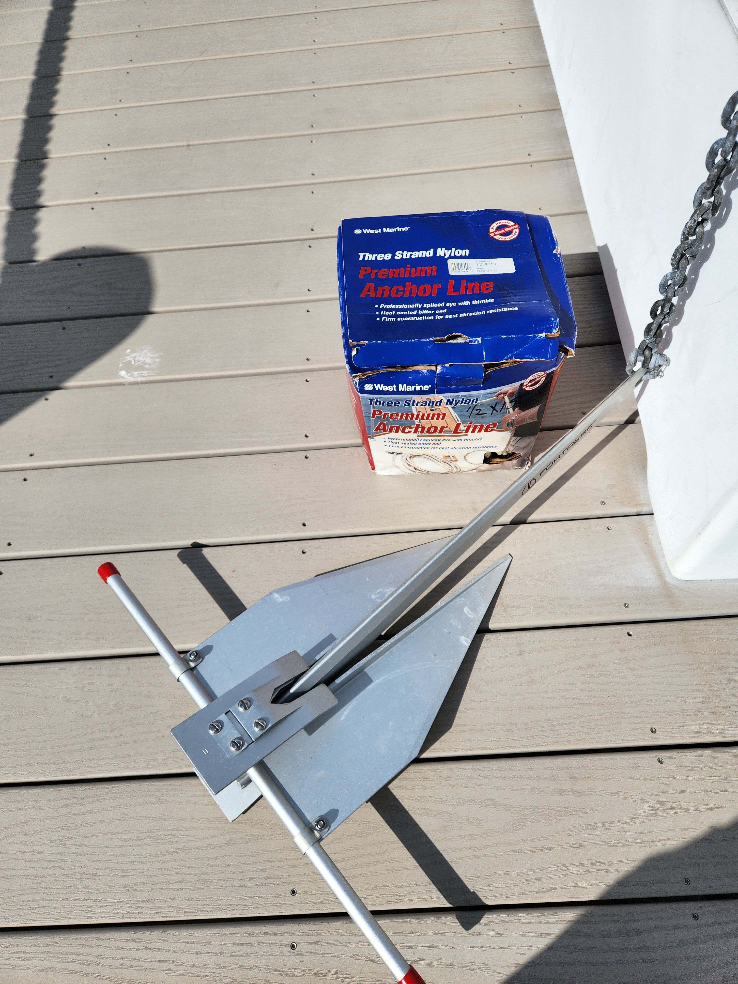 An anchor and chain lie on a boat dock next to a box of anchor line.