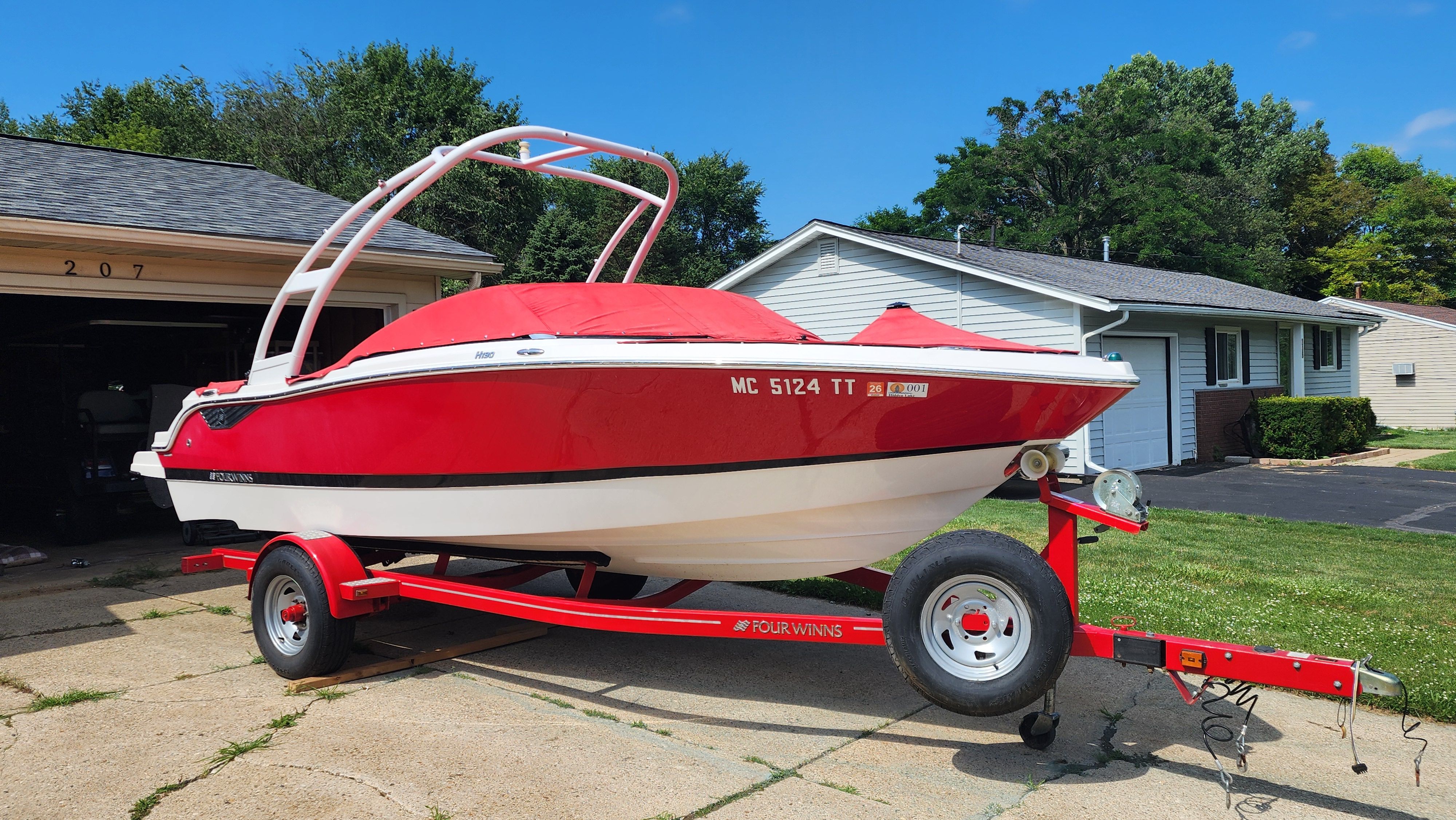 A red 2015 Four Winns H190 boat on a trailer in a driveway.