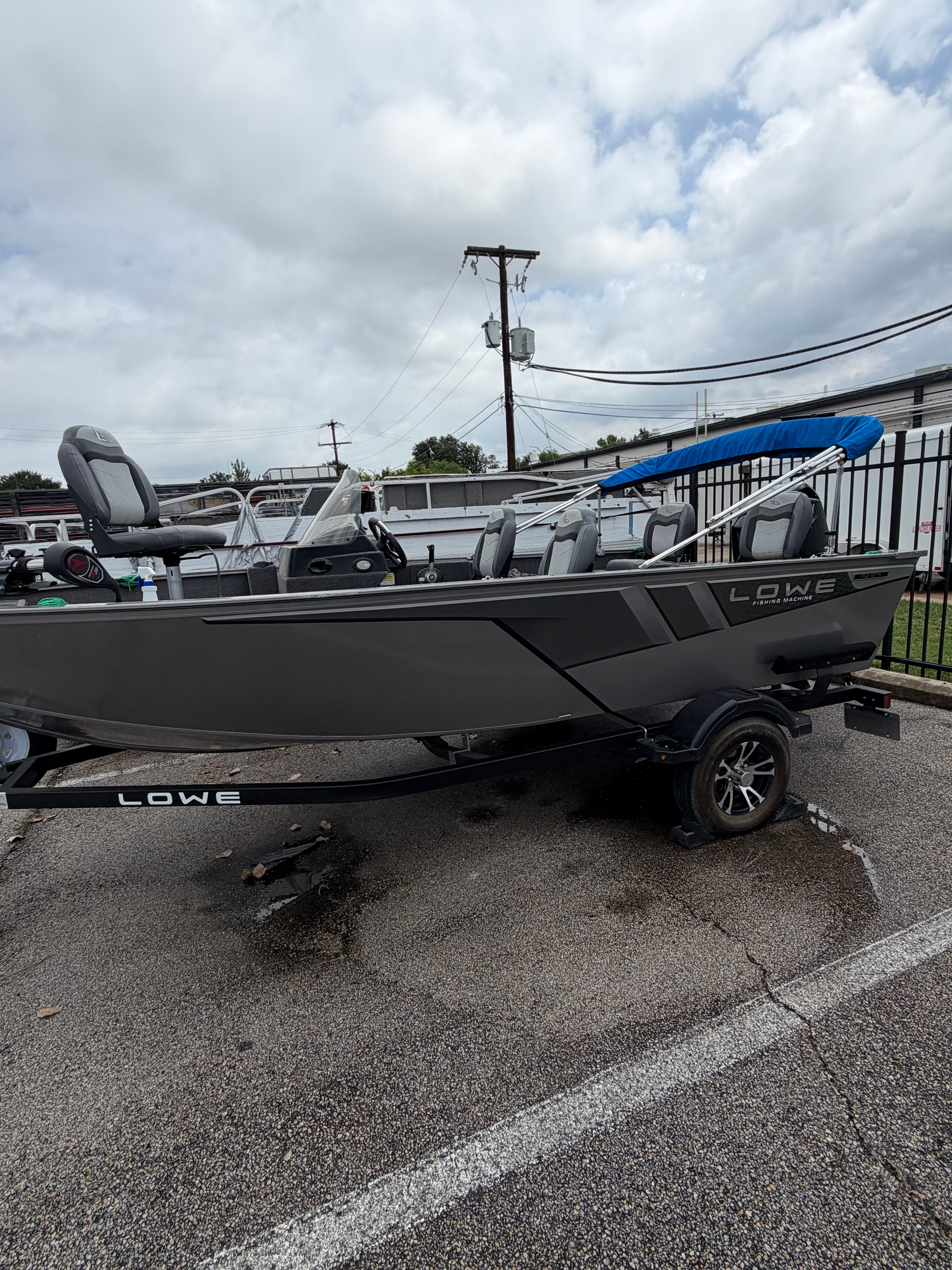 A gray 2023 Lowe Fishing Machine 1675SC boat on a trailer in a parking lot.