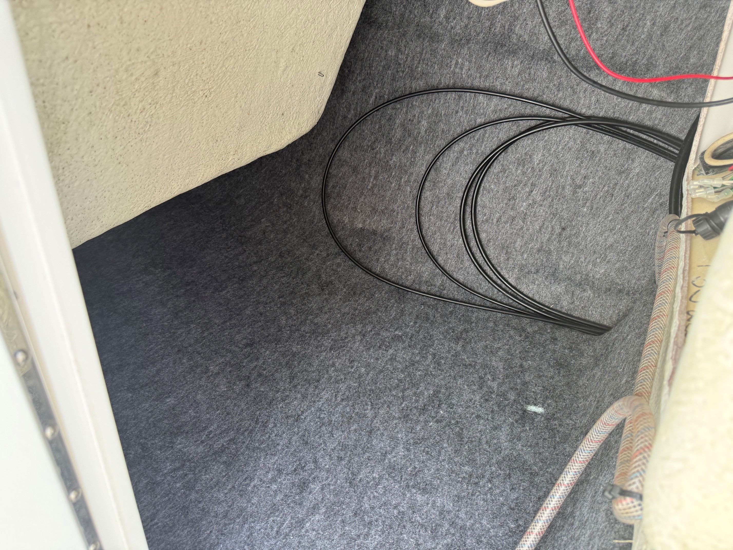 Interior of a boat with gray carpet flooring and cables.