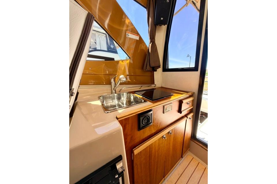 2017 Cutwater C-242 Coupe interior kitchen with sink, stove, and wooden cabinetry.