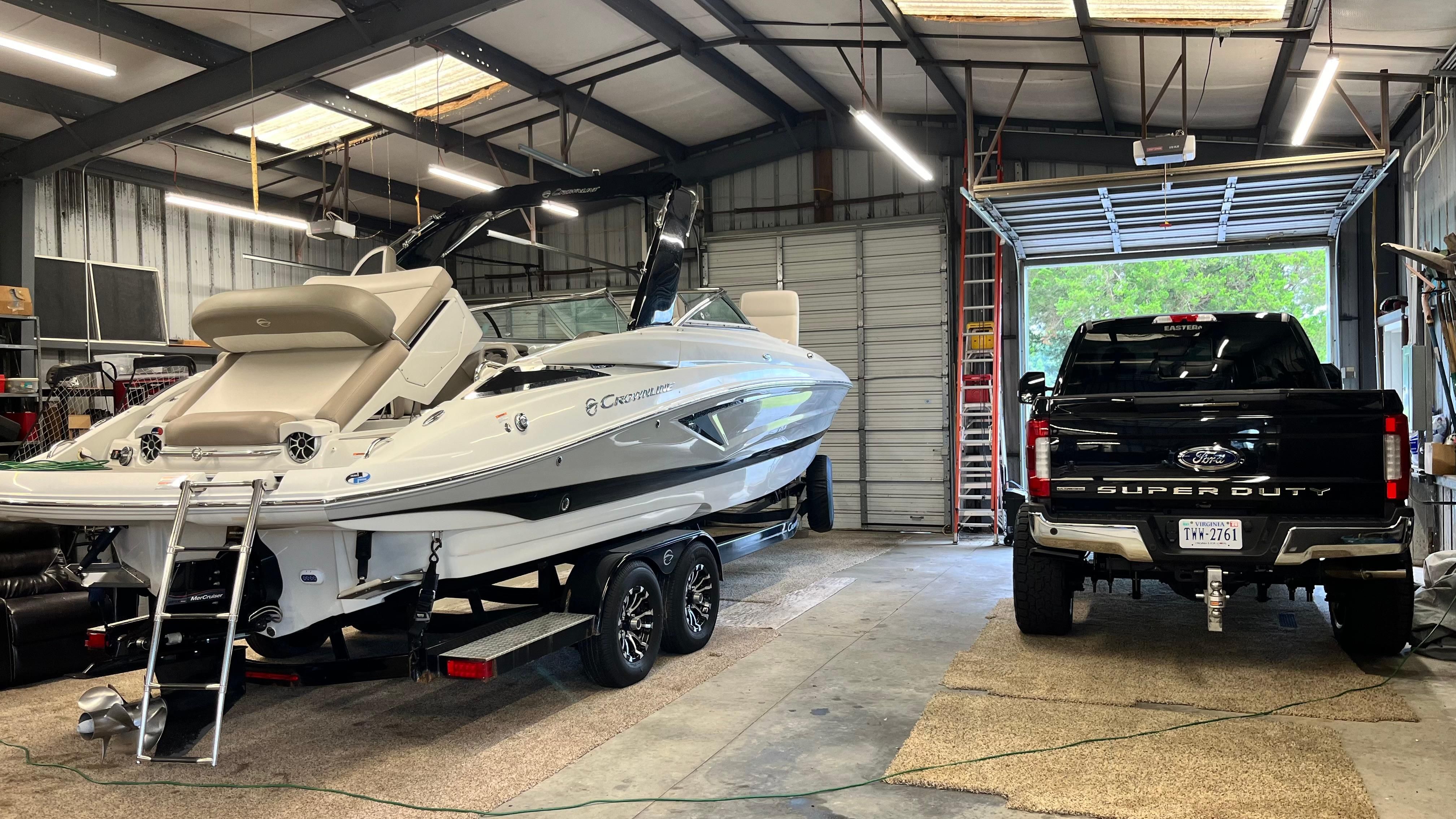 A 2019 Crownline E 285 is in a garage next to a black pickup truck.