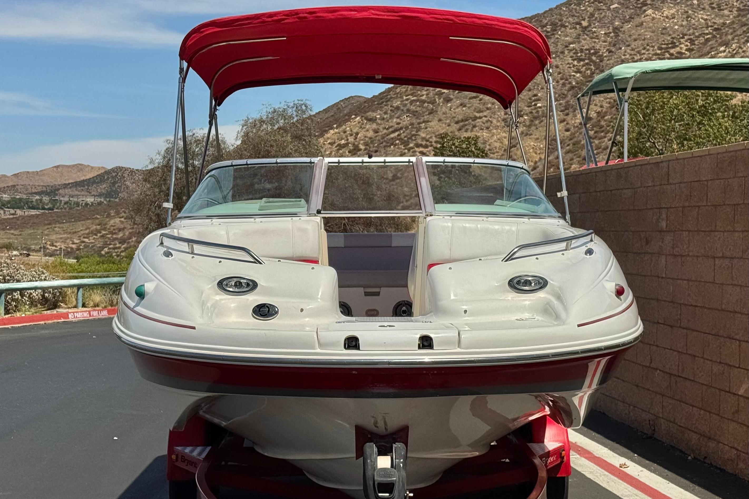 2010 Bryant 255 boat with red canopy, parked on a sunny day near hills.