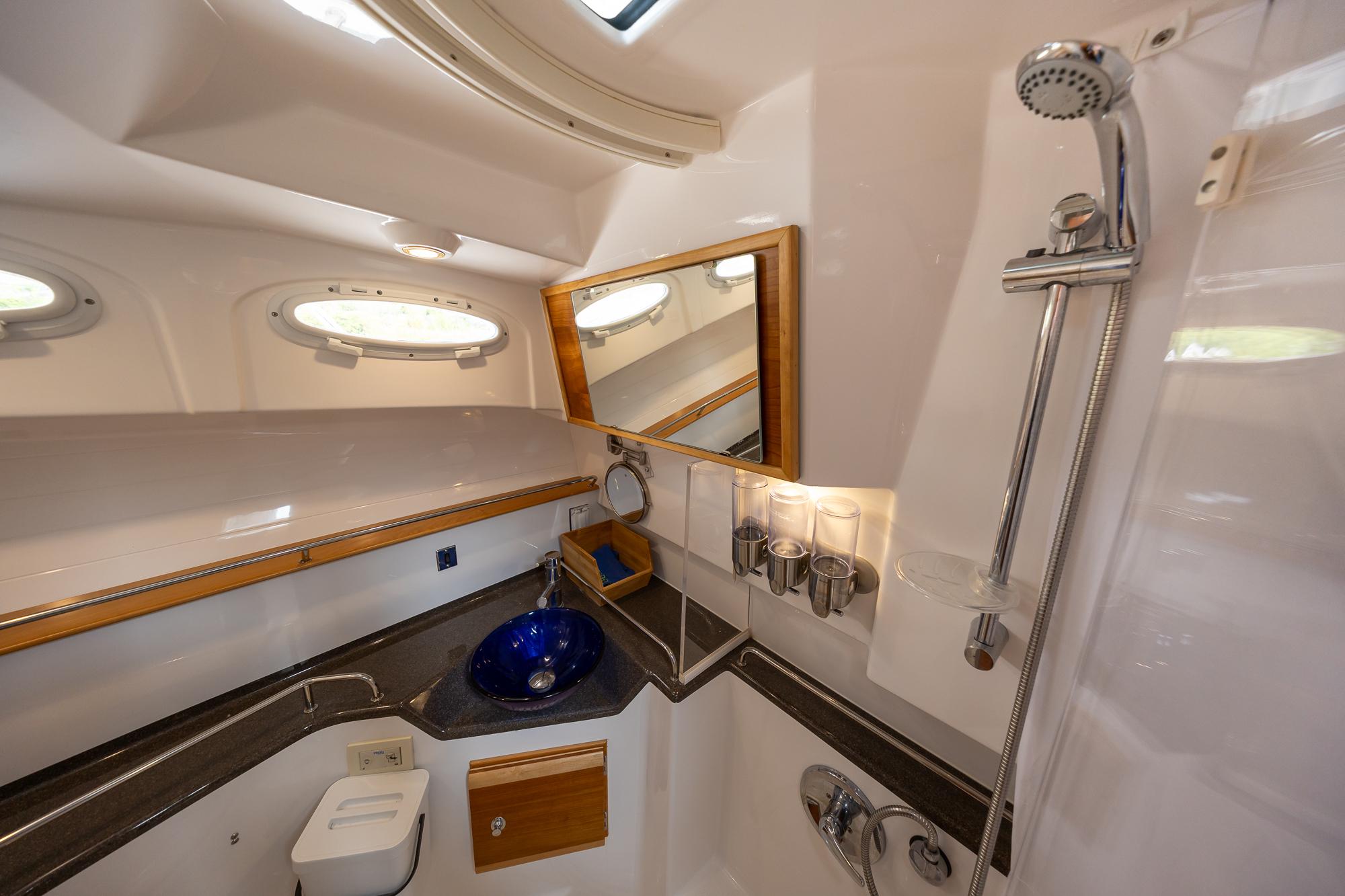 2017 Cutwater C-302 Sport Coupe bathroom with shower, blue sink, and porthole windows.
