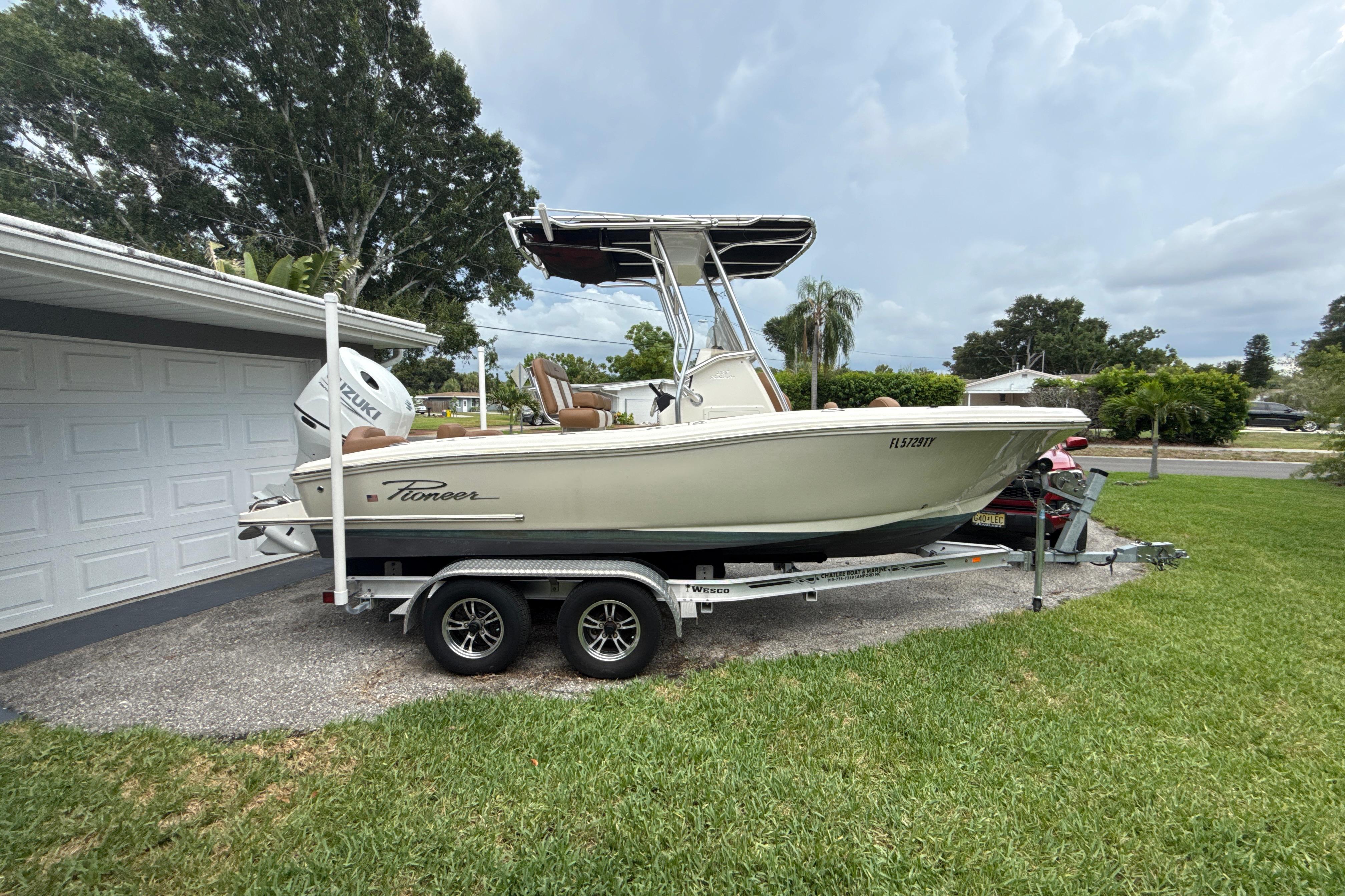 2023 Pioneer 202 Islander boat on trailer, parked beside a garage, with lush greenery.