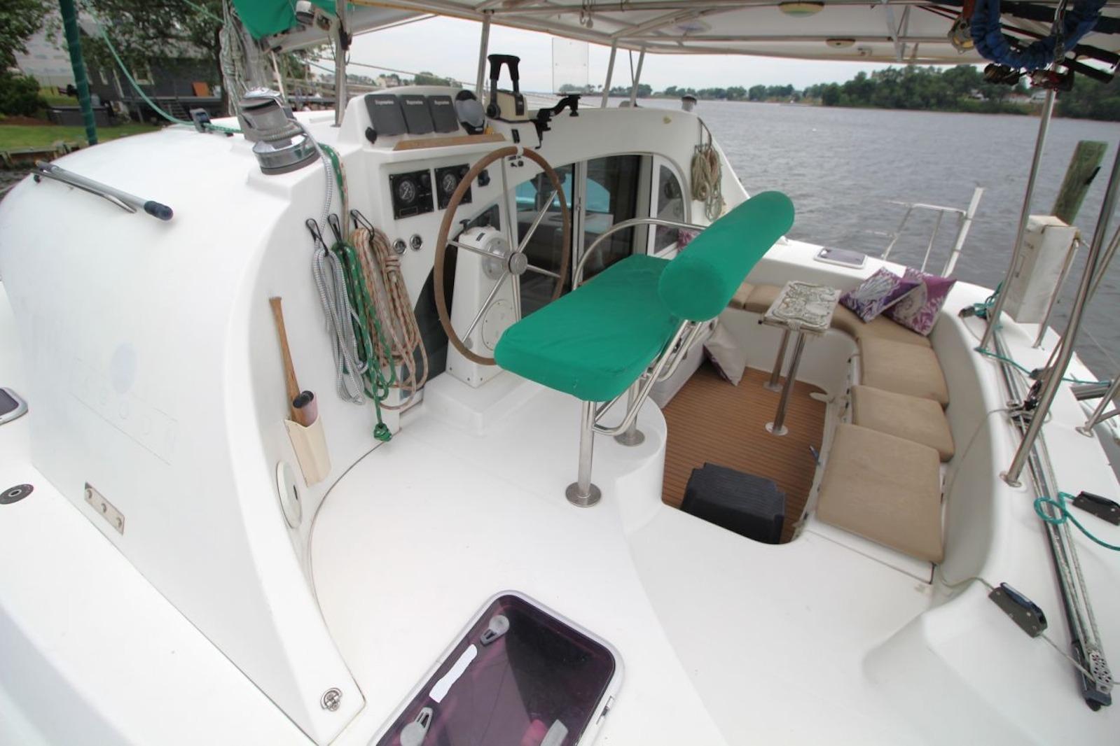 2004 Lagoon 380 catamaran cockpit with green seating, steering wheel, and spacious lounging area.