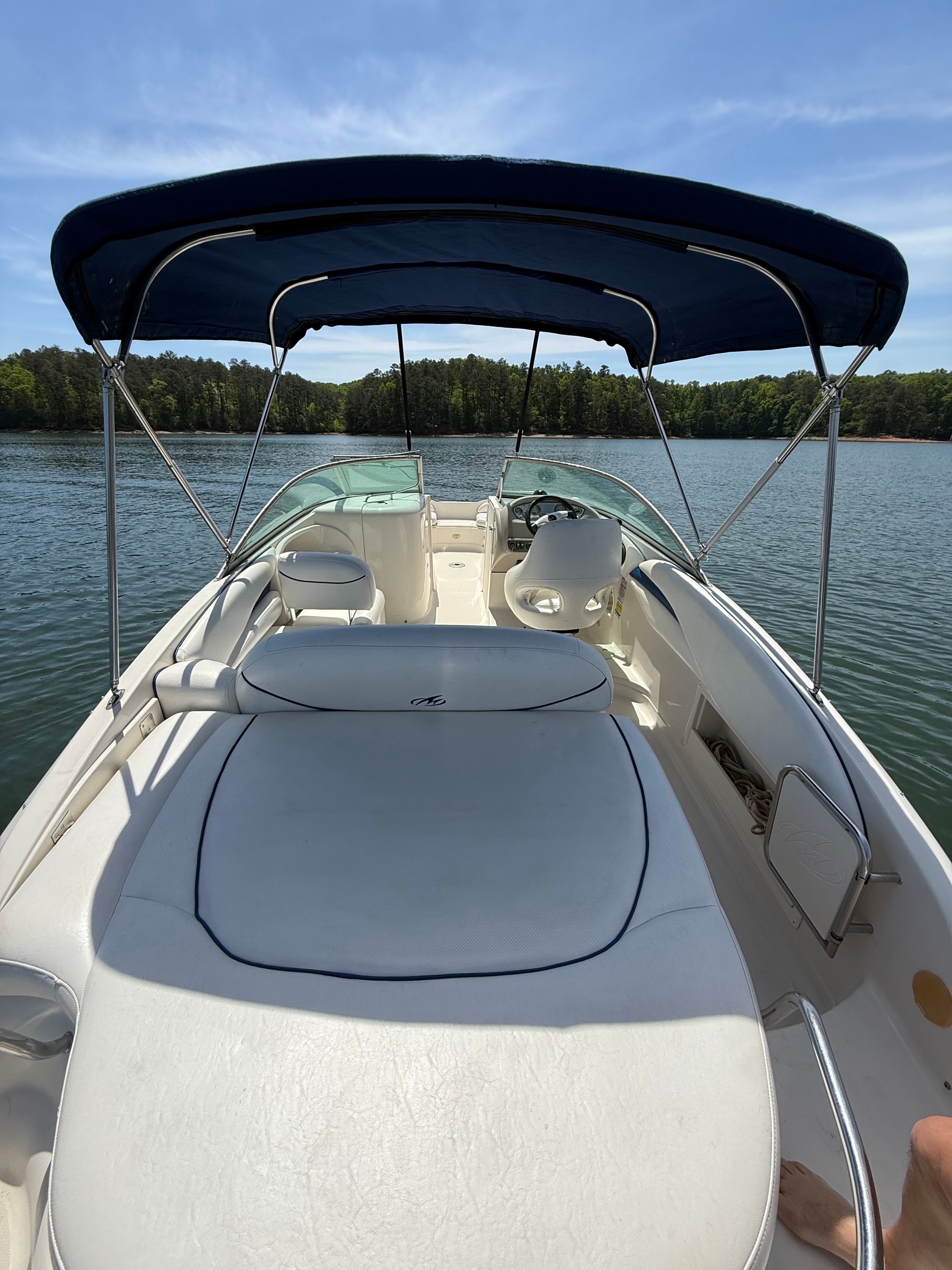 A 2005 Monterey 223 Explorer Sport on a calm lake with a blue sunshade.