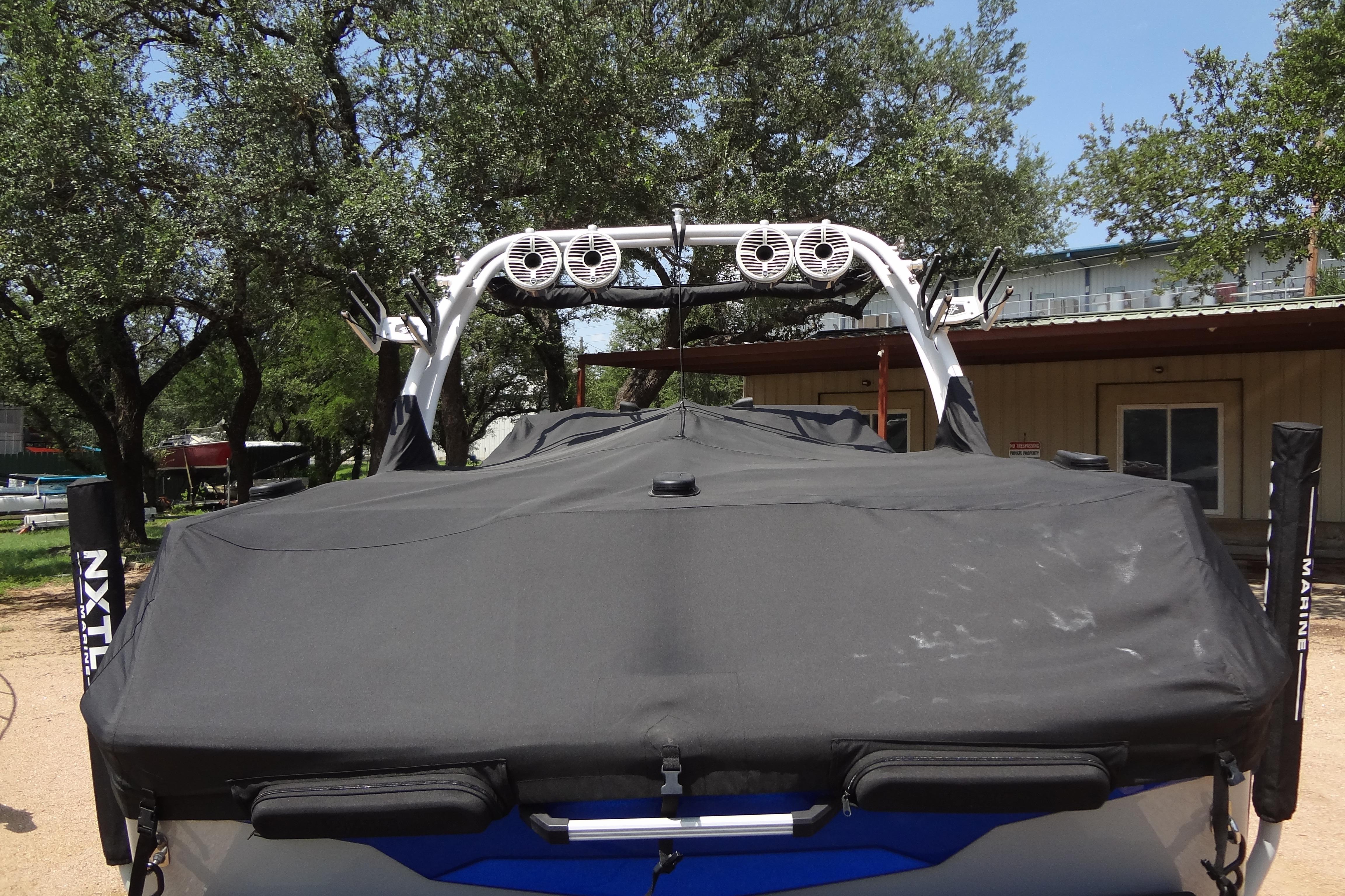 2022 ATX Surf Boats 24 Type-S covered, parked outdoors with trees and building in background.