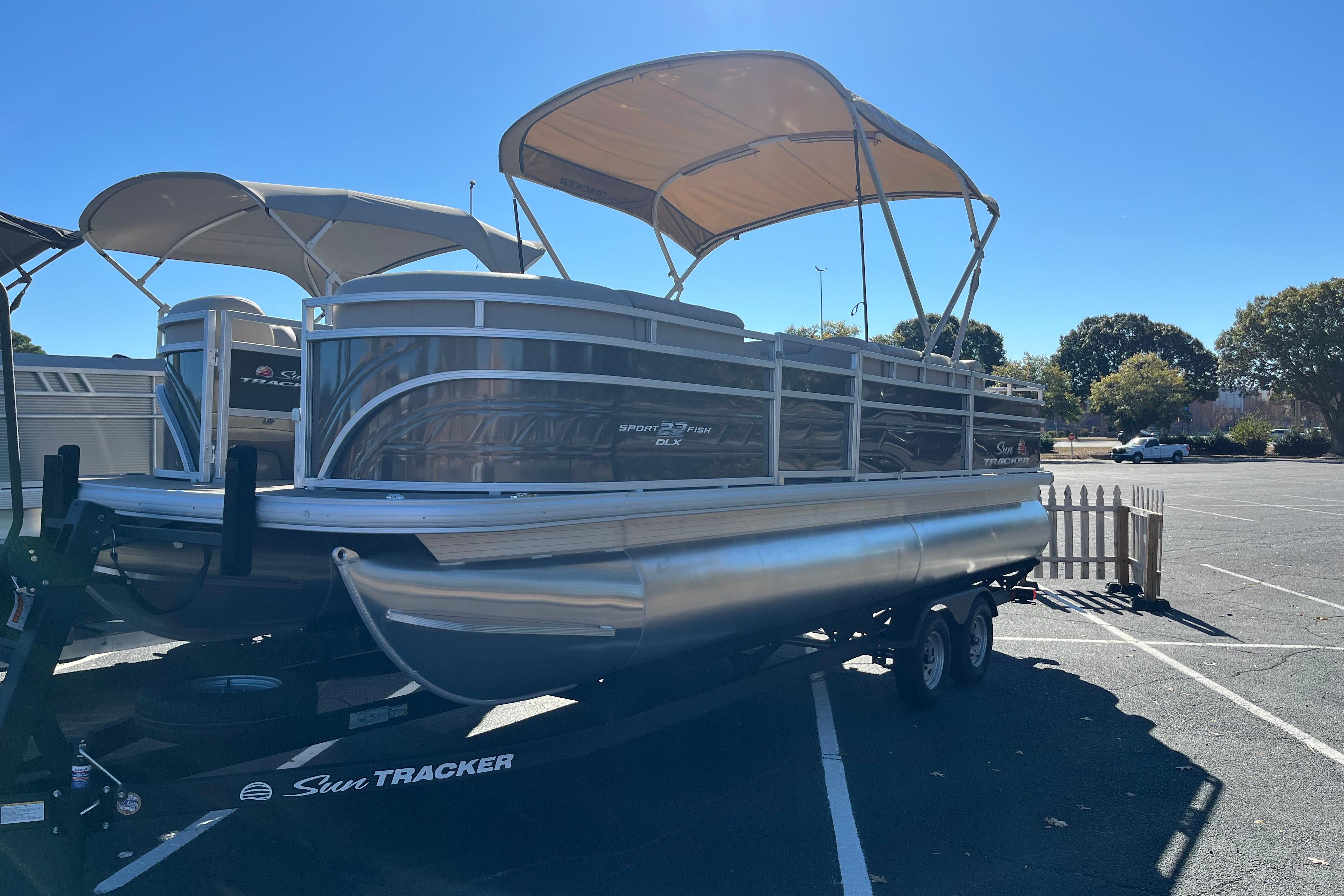 2025 Sun Tracker SportFish 22 DLX pontoon boat on trailer in parking lot.