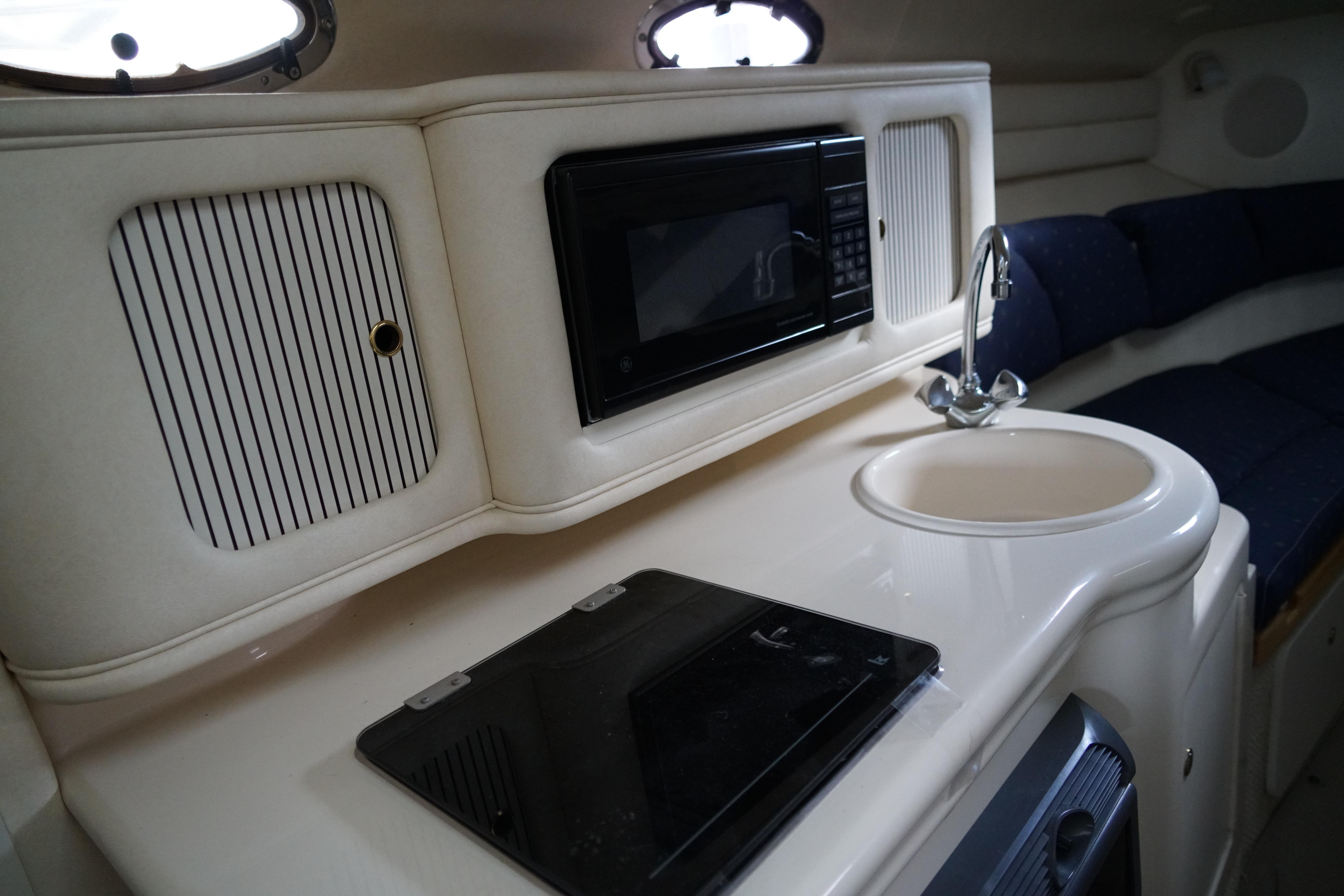 2002 Sea Ray Sundancer 260 interior with kitchenette, featuring a microwave, sink, and stove.