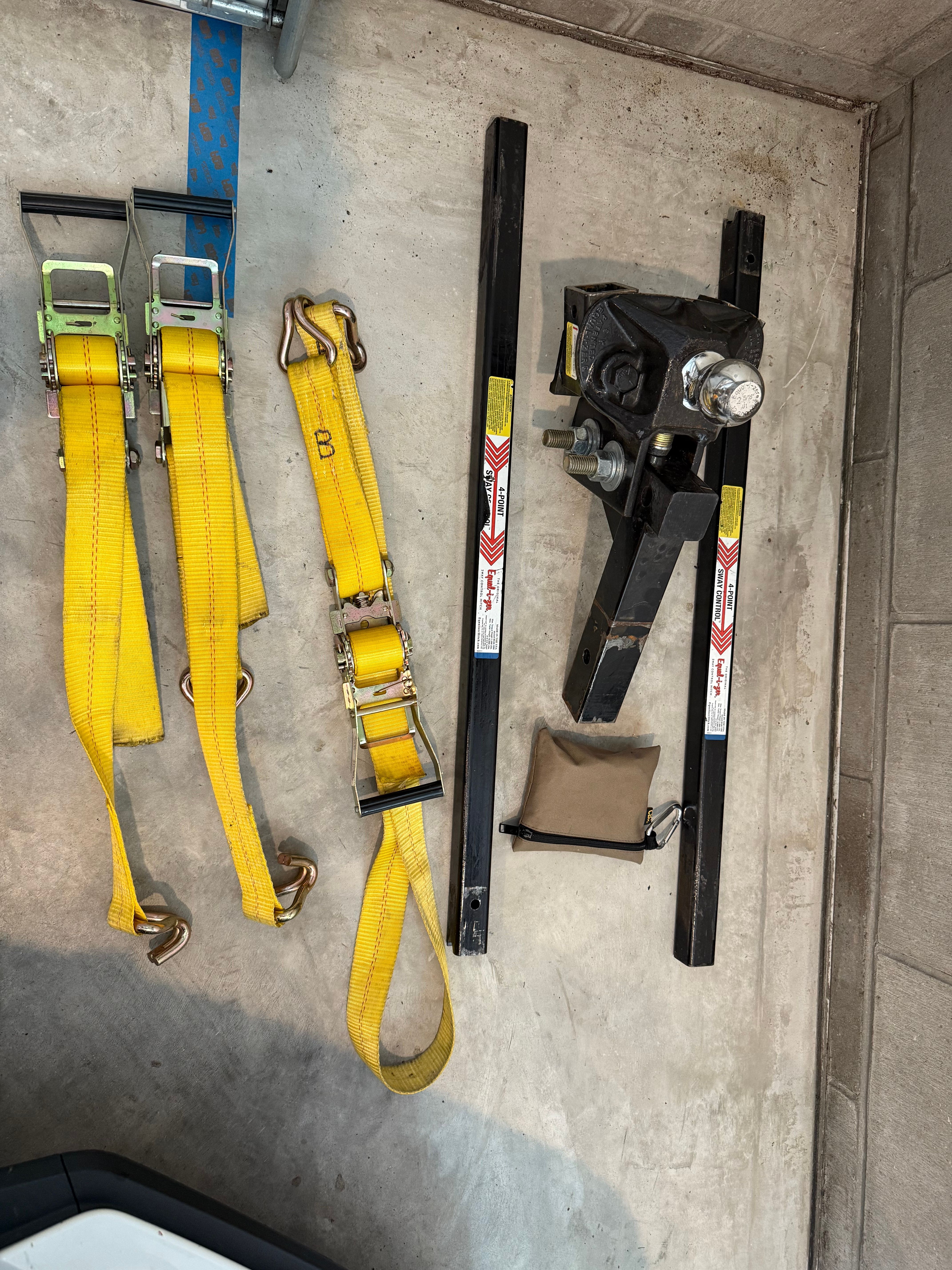 Yellow tie-down straps and hitch components on concrete floor.