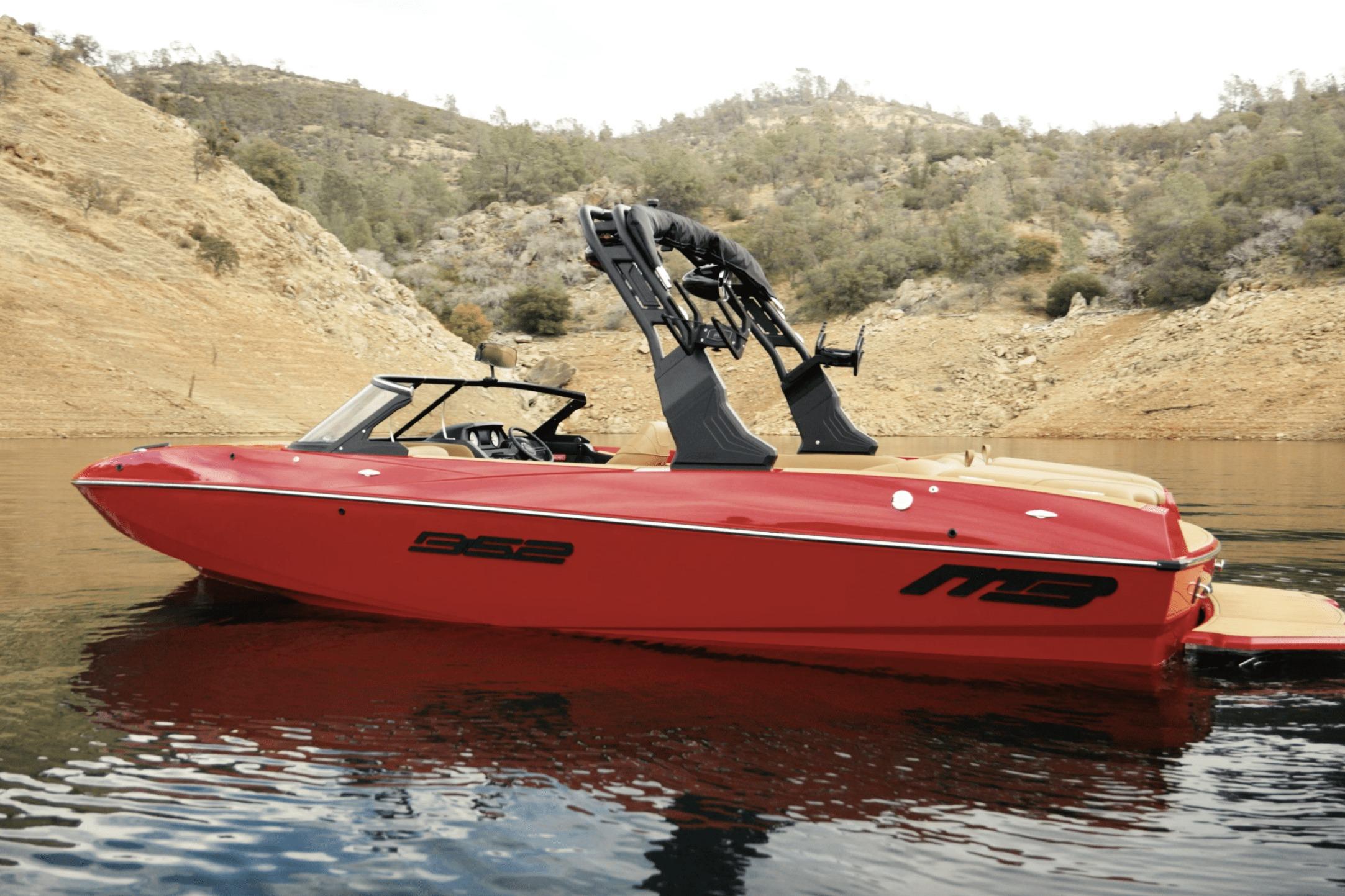 Red 2027 MB B52 23 Classic boat on calm lake with rocky shoreline backdrop.