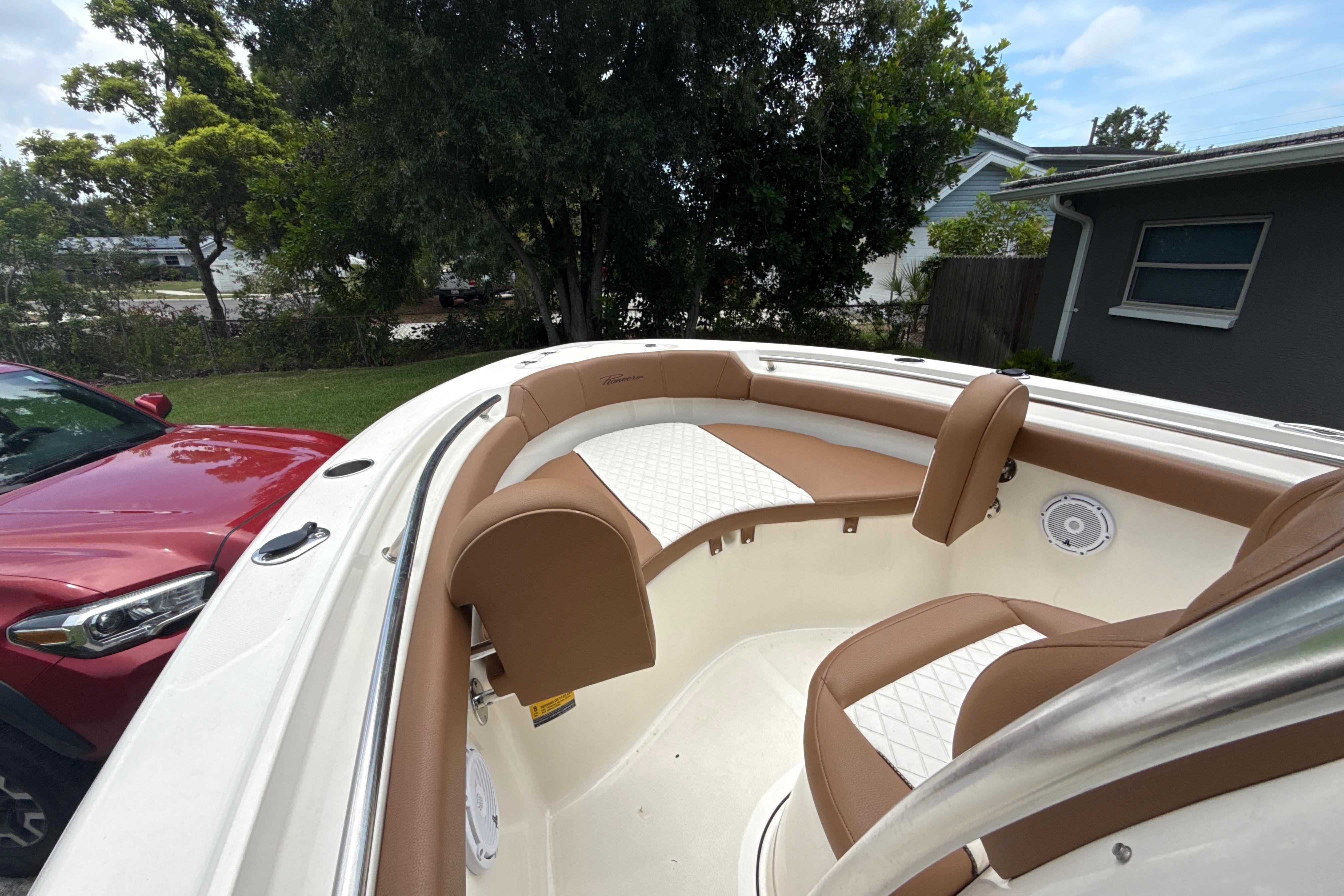 2023 Pioneer 202 Islander boat interior with brown and white seating, parked near a red car.