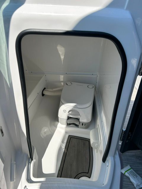 A modern boat toilet in a white, compact space with a wooden floor.