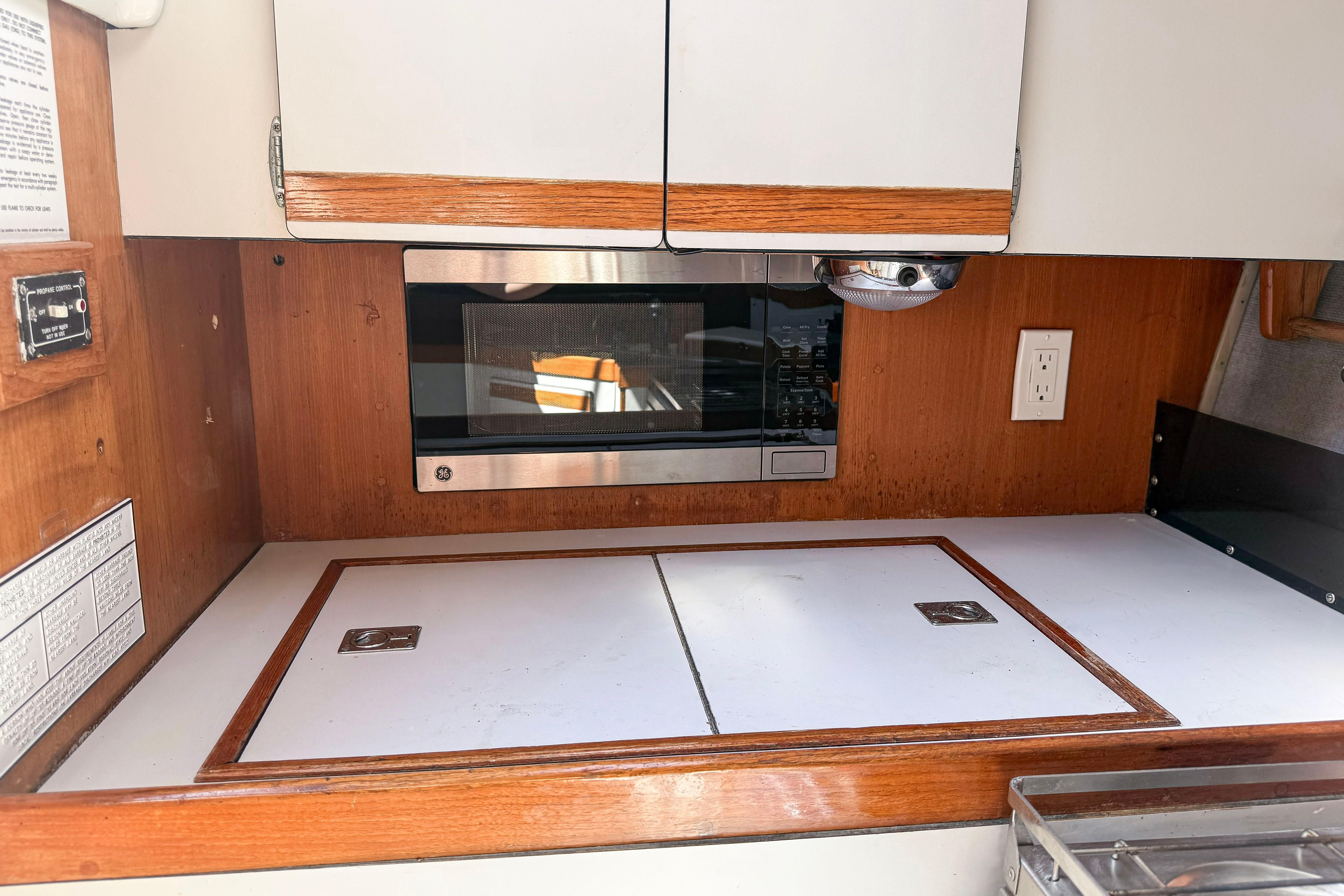 1988 Oday 40 yacht galley with microwave, wooden cabinetry, and white countertop.