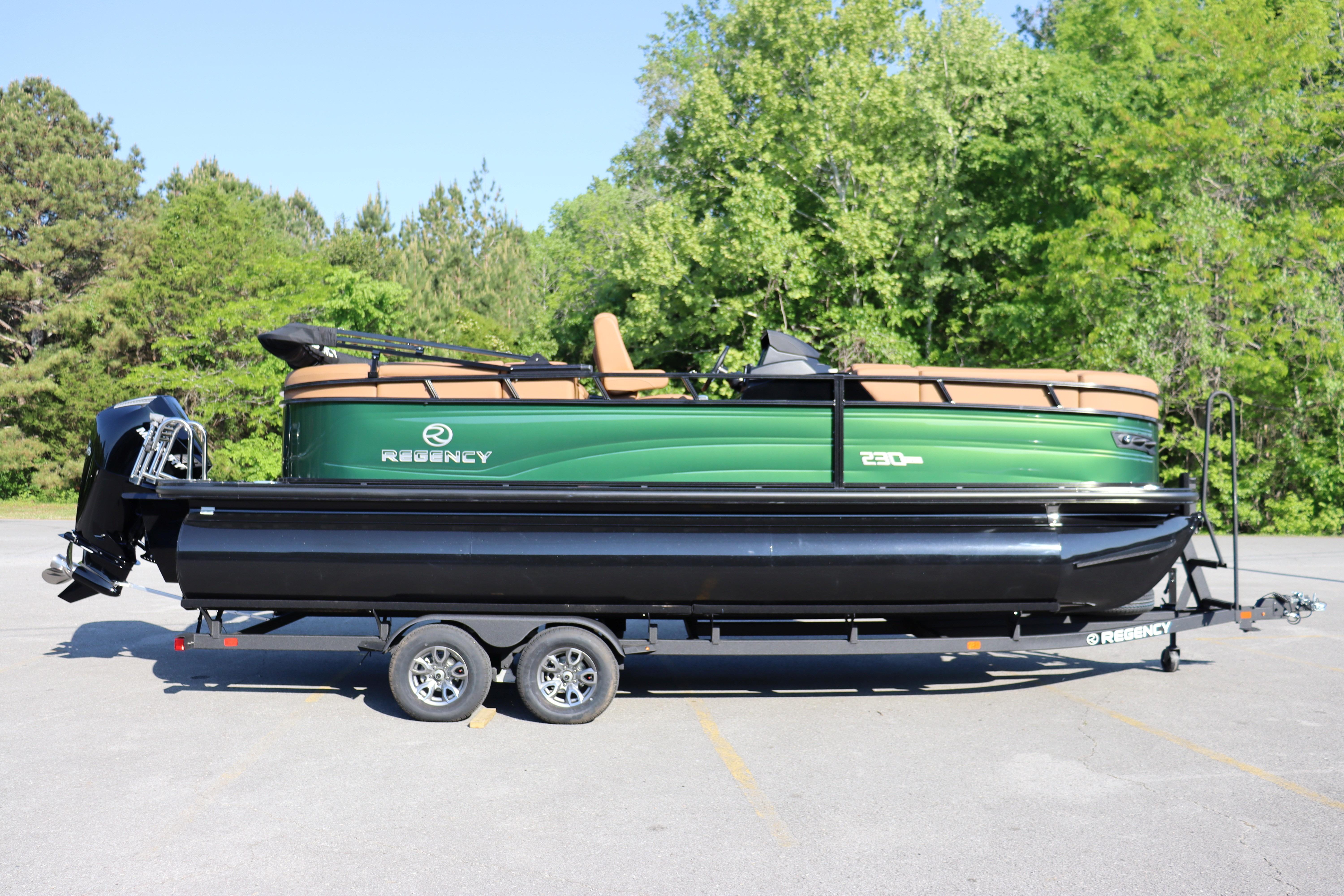 2026 Regency 230 DL pontoon boat on trailer, parked outdoors with lush green trees.