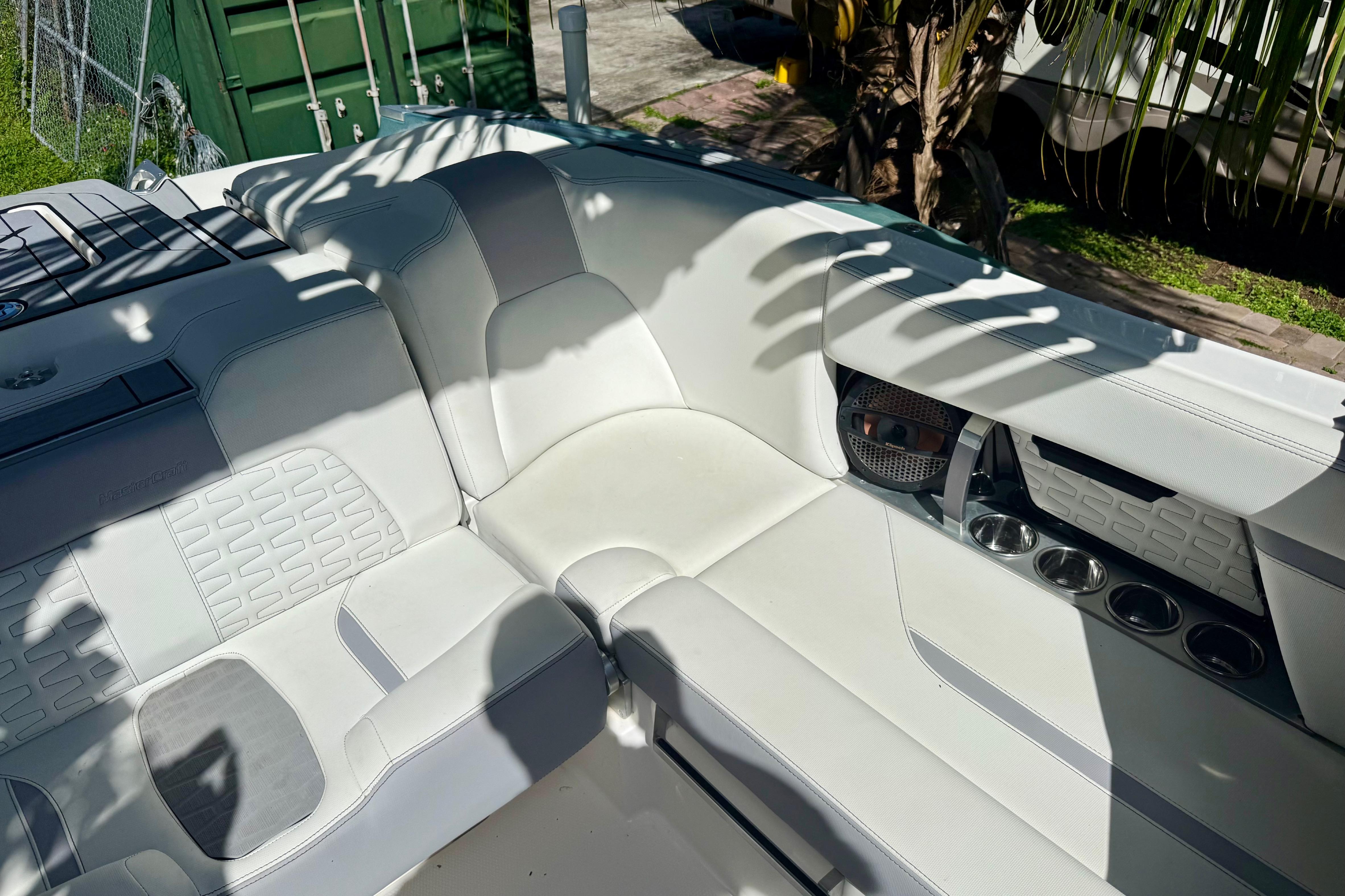2023 MasterCraft X24 boat interior with white seating and cup holders, shaded by palm leaves.