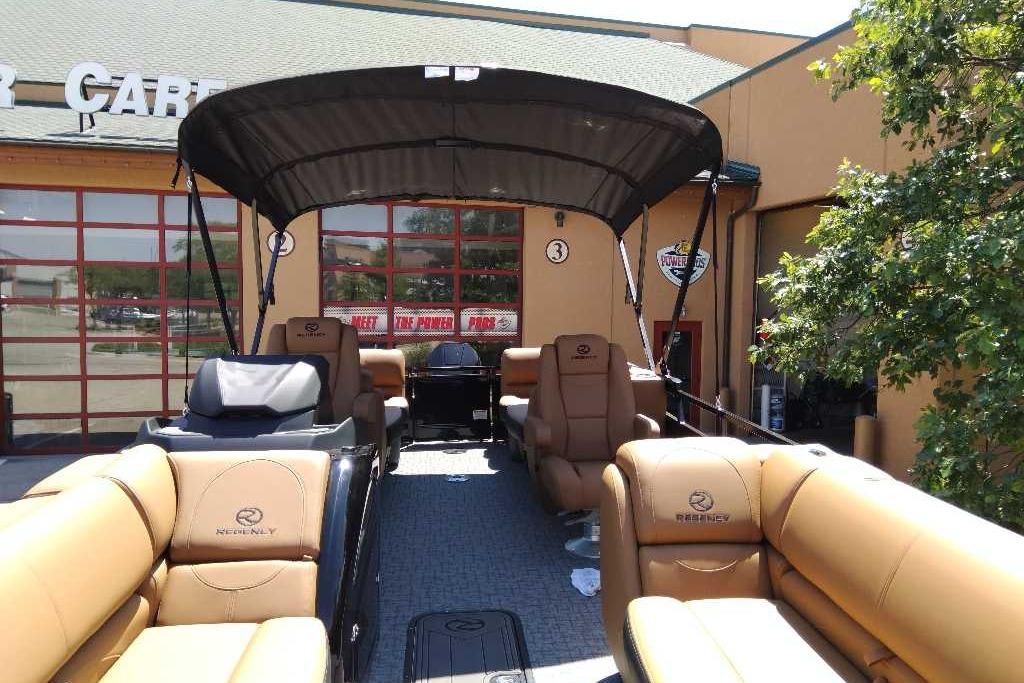 2026 Regency 230 DL pontoon boat with tan seating and canopy, displayed outdoors.