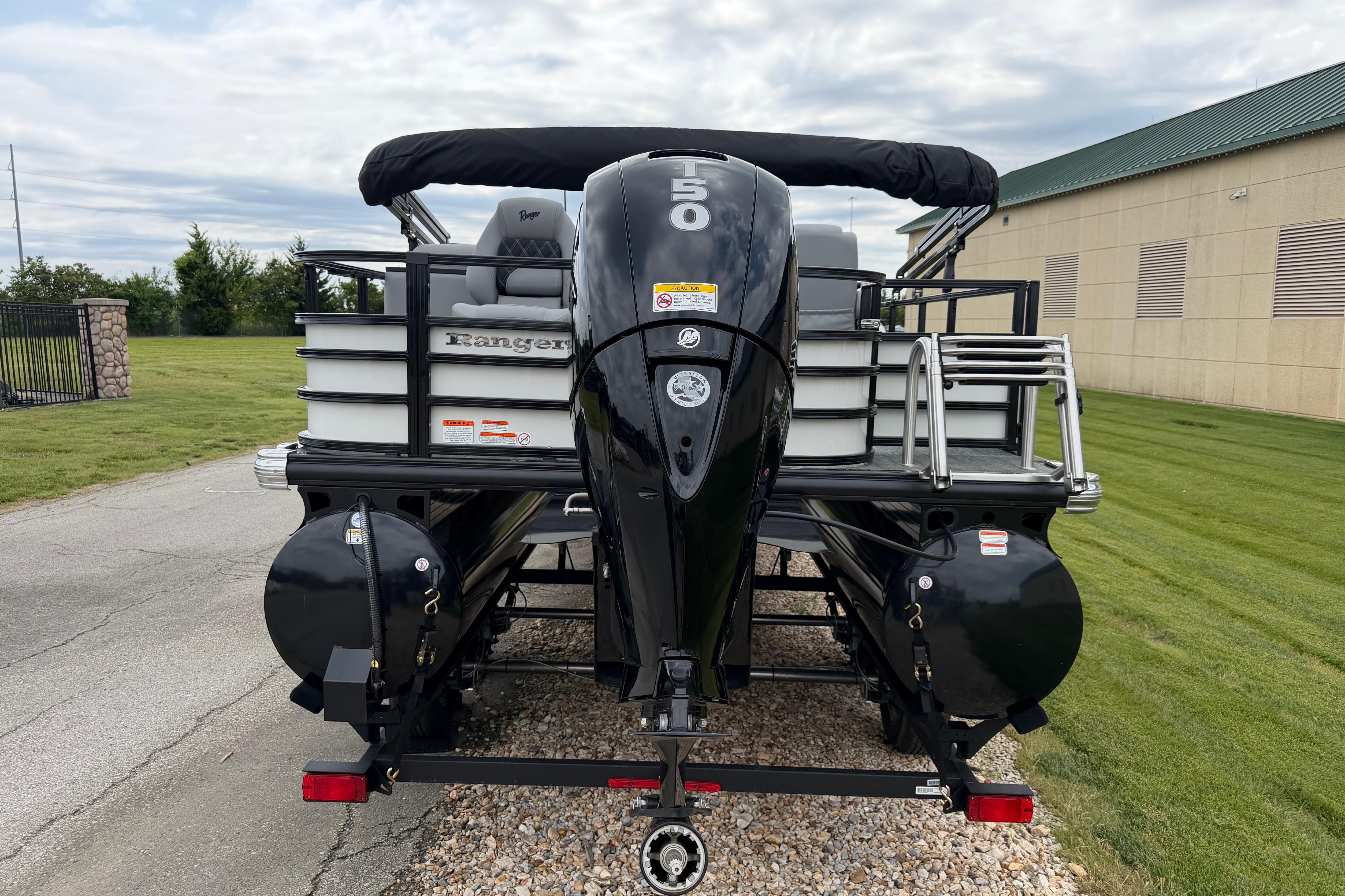 2026 Ranger 220FC boat with powerful outboard motor, parked on gravel near a building.