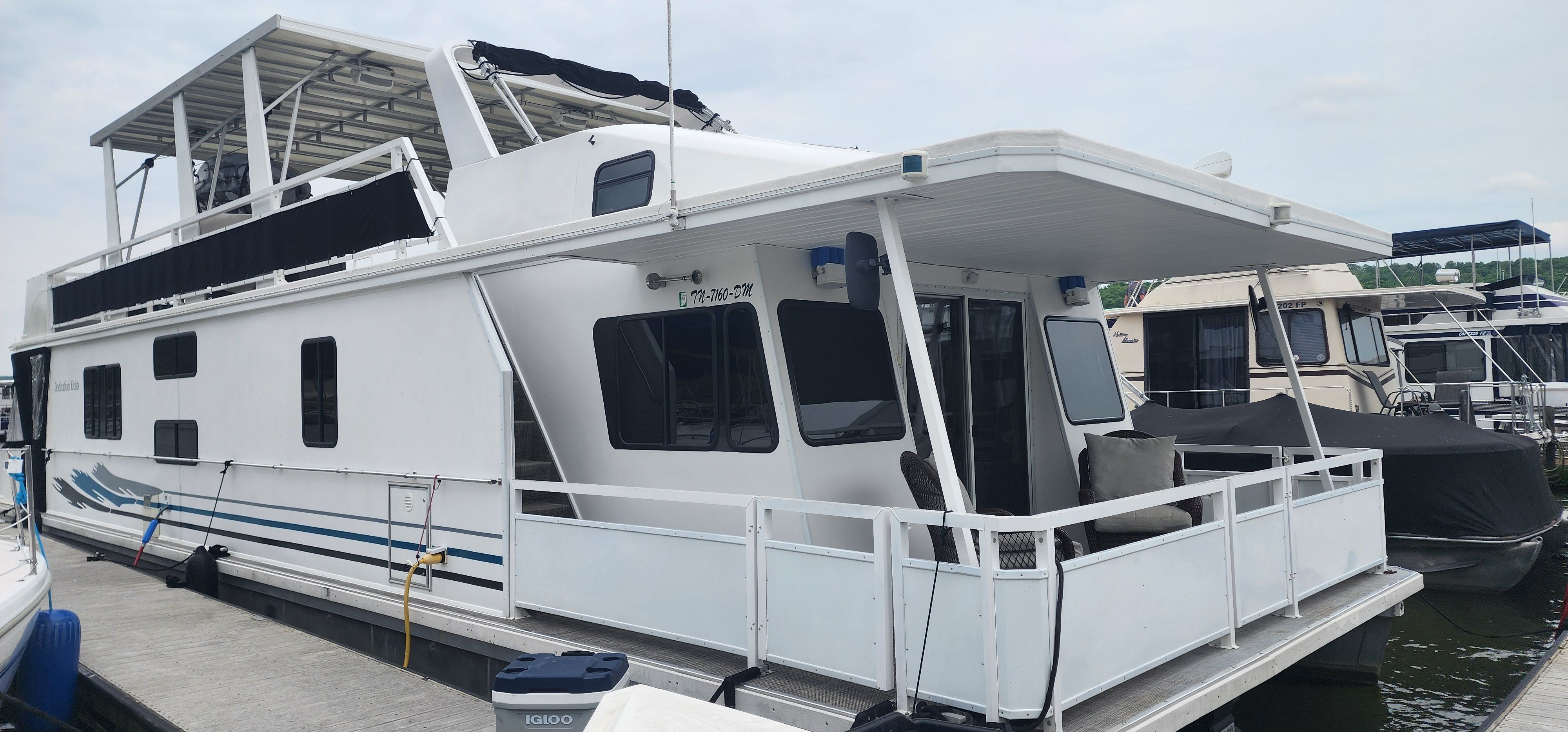 Houseboat with covered deck and seating area, docked at a marina.
