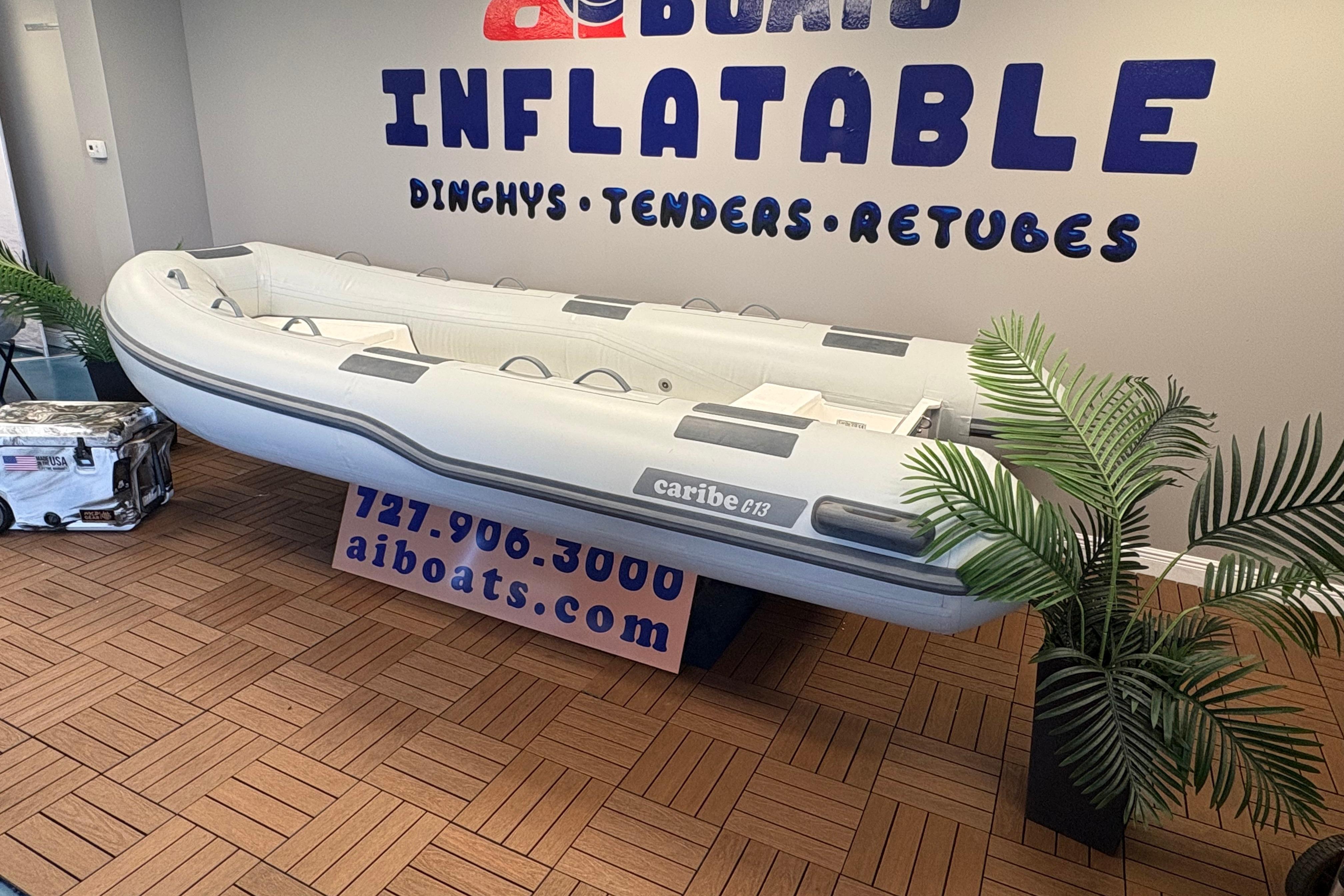 Inflatable Caribe C-13 boat displayed indoors, 2026 model, with promotional signage and plants.