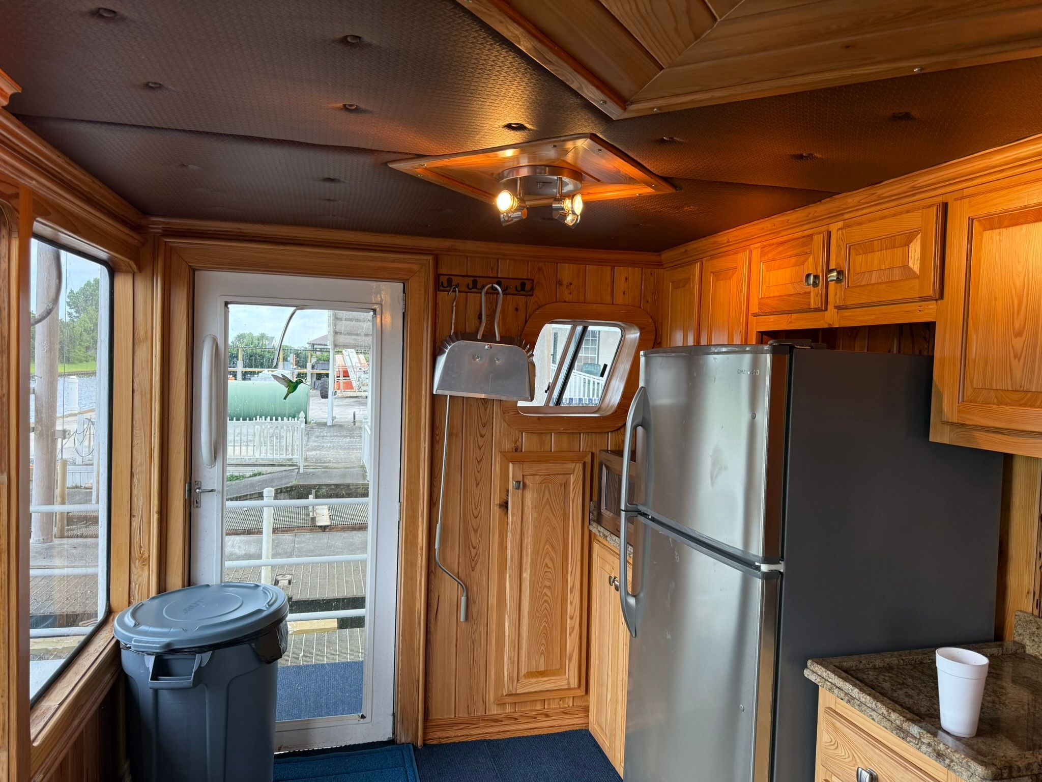 Interior of a boat kitchen with wood paneling, stainless steel fridge, and windows overlooking the harbor.