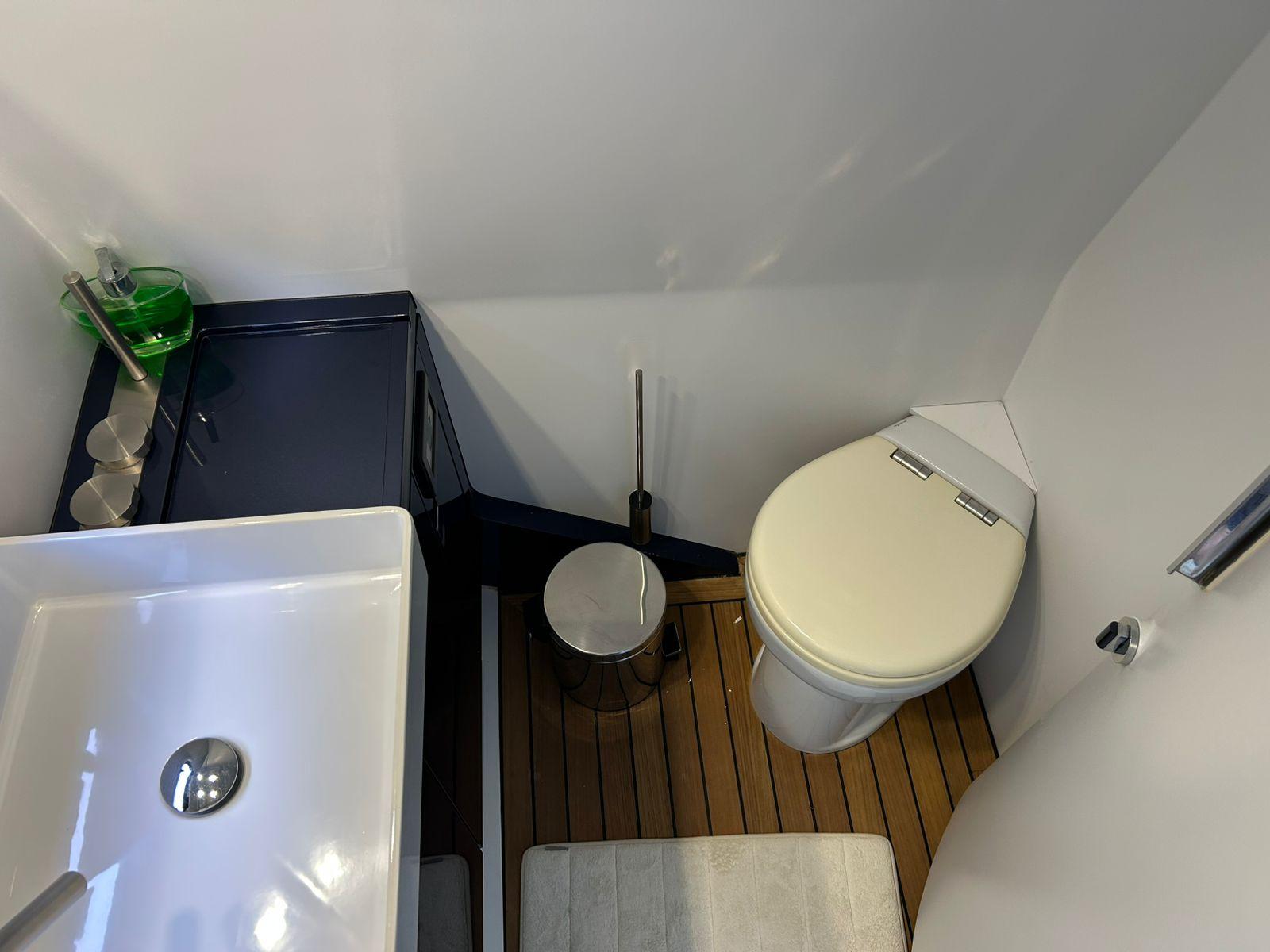 Compact bathroom in a 2016 Maori 50 yacht, featuring a sink, toilet, and wooden flooring.