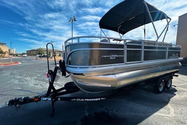 2025 Sun Tracker Fishin' Barge 20 DLX pontoon boat on trailer, parked outdoors.