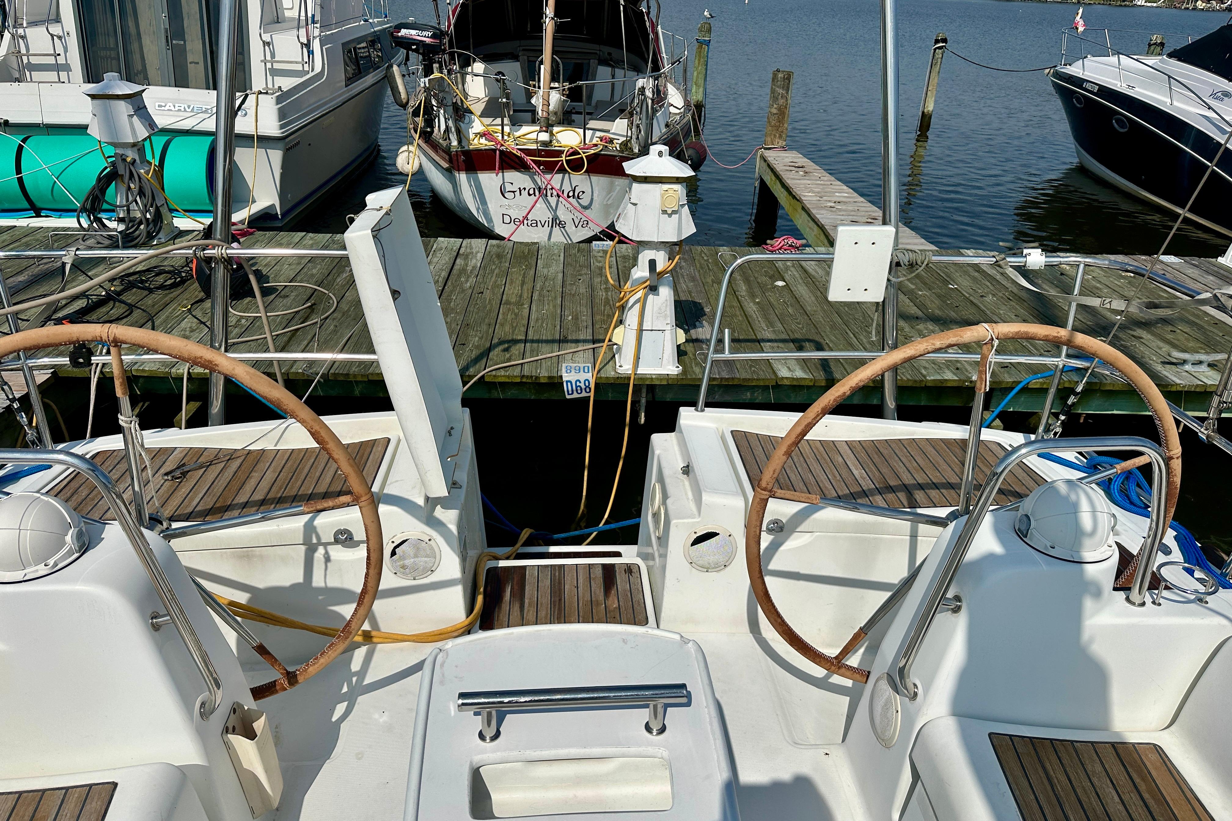 2010 Beneteau Oceanis 40 sailboat docked, featuring dual steering wheels and wooden deck.