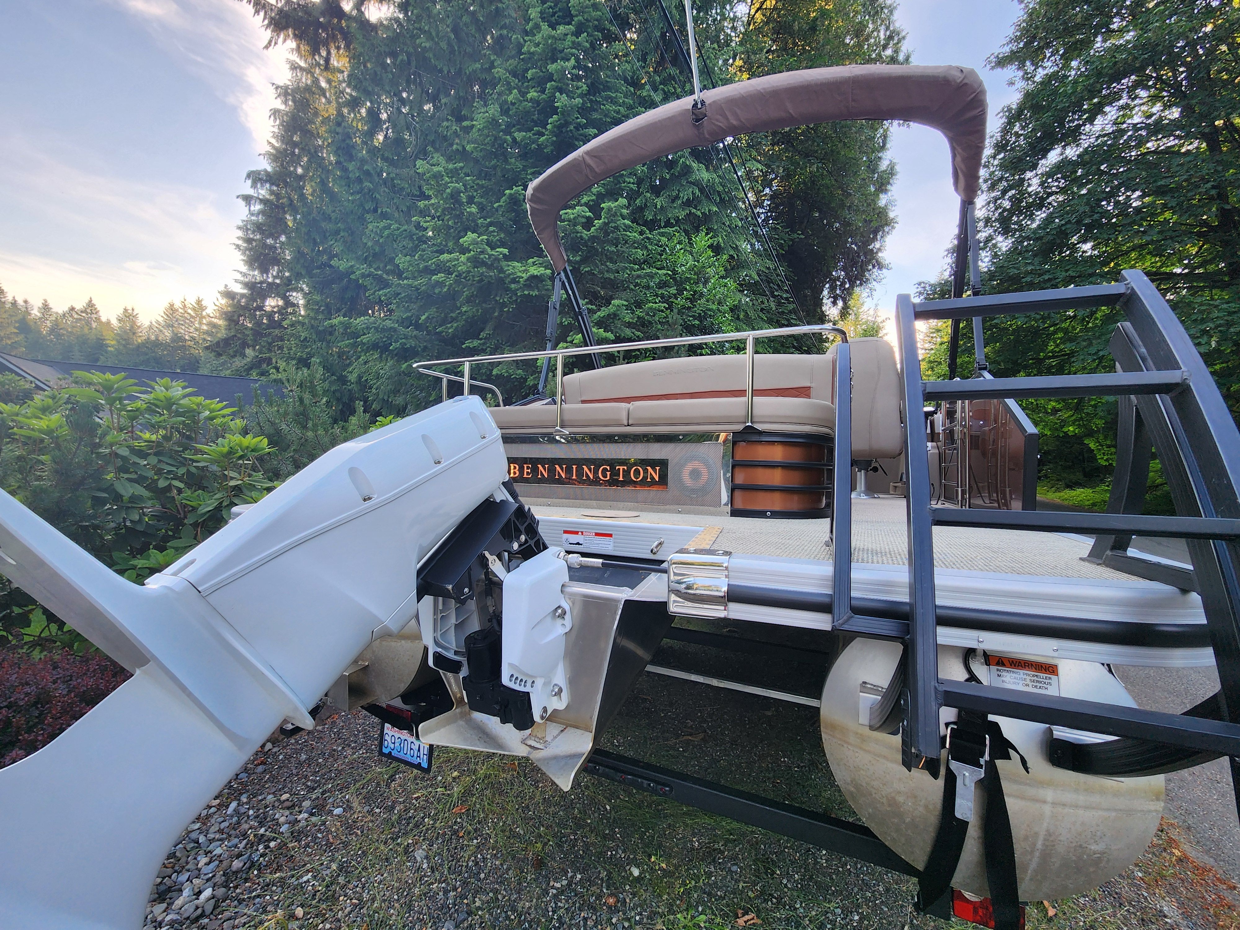 A 2023 Bennington 22 LSB pontoon boat on a trailer, surrounded by trees.