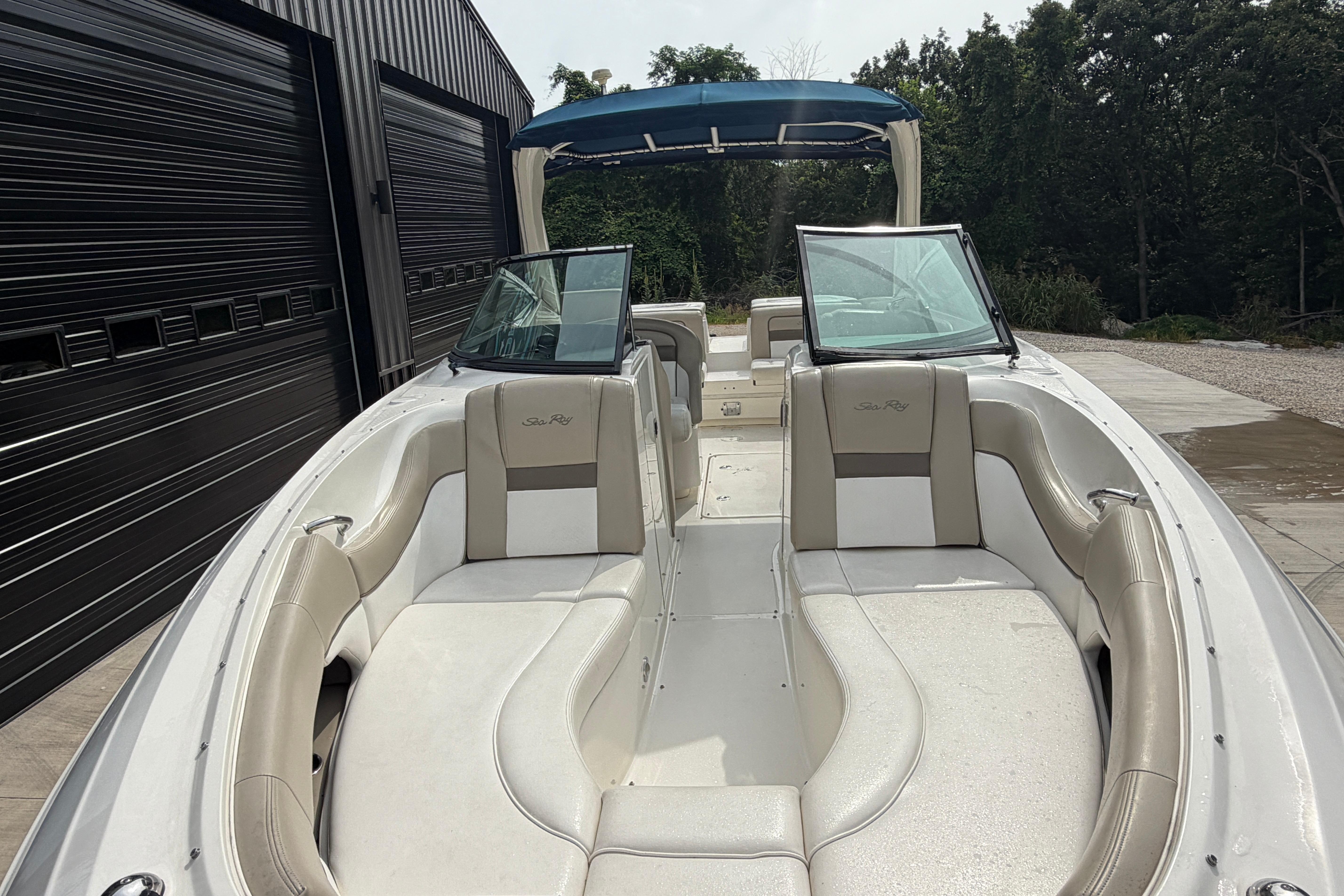2013 Sea Ray 300 SLX boat with beige seating and blue canopy, parked near a garage.