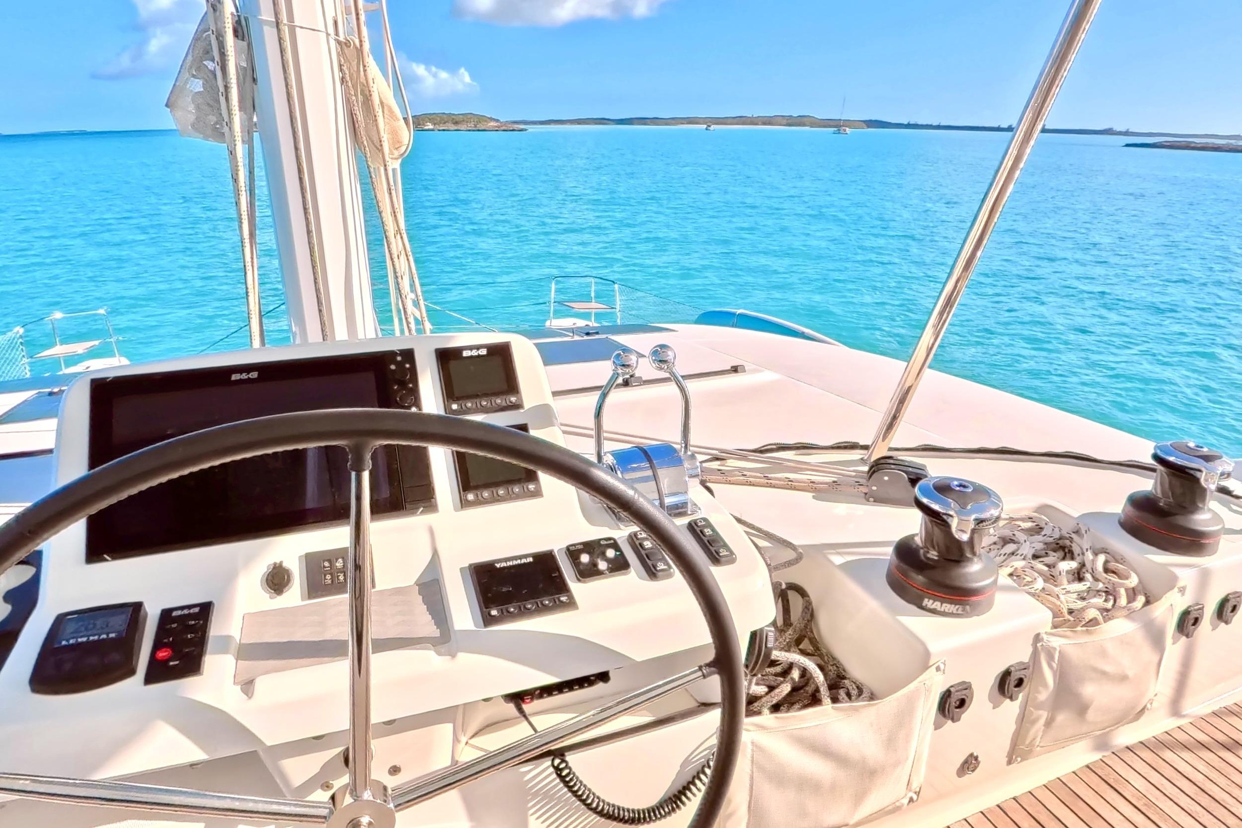 Steering wheel and controls of 2023 Lagoon 50 catamaran on clear blue water.