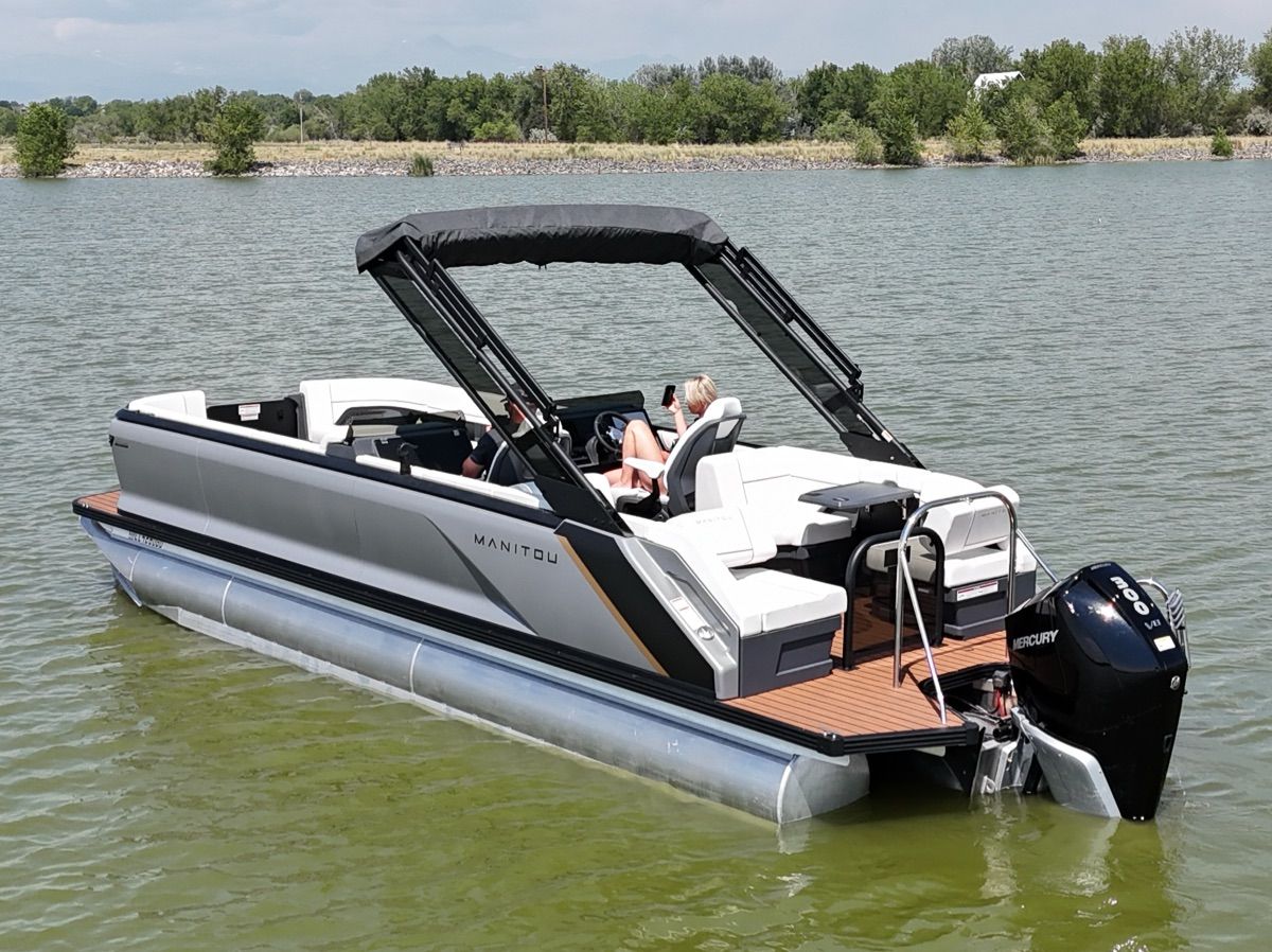 A modern pontoon boat by Manitou, model Explore 2024, on calm water.