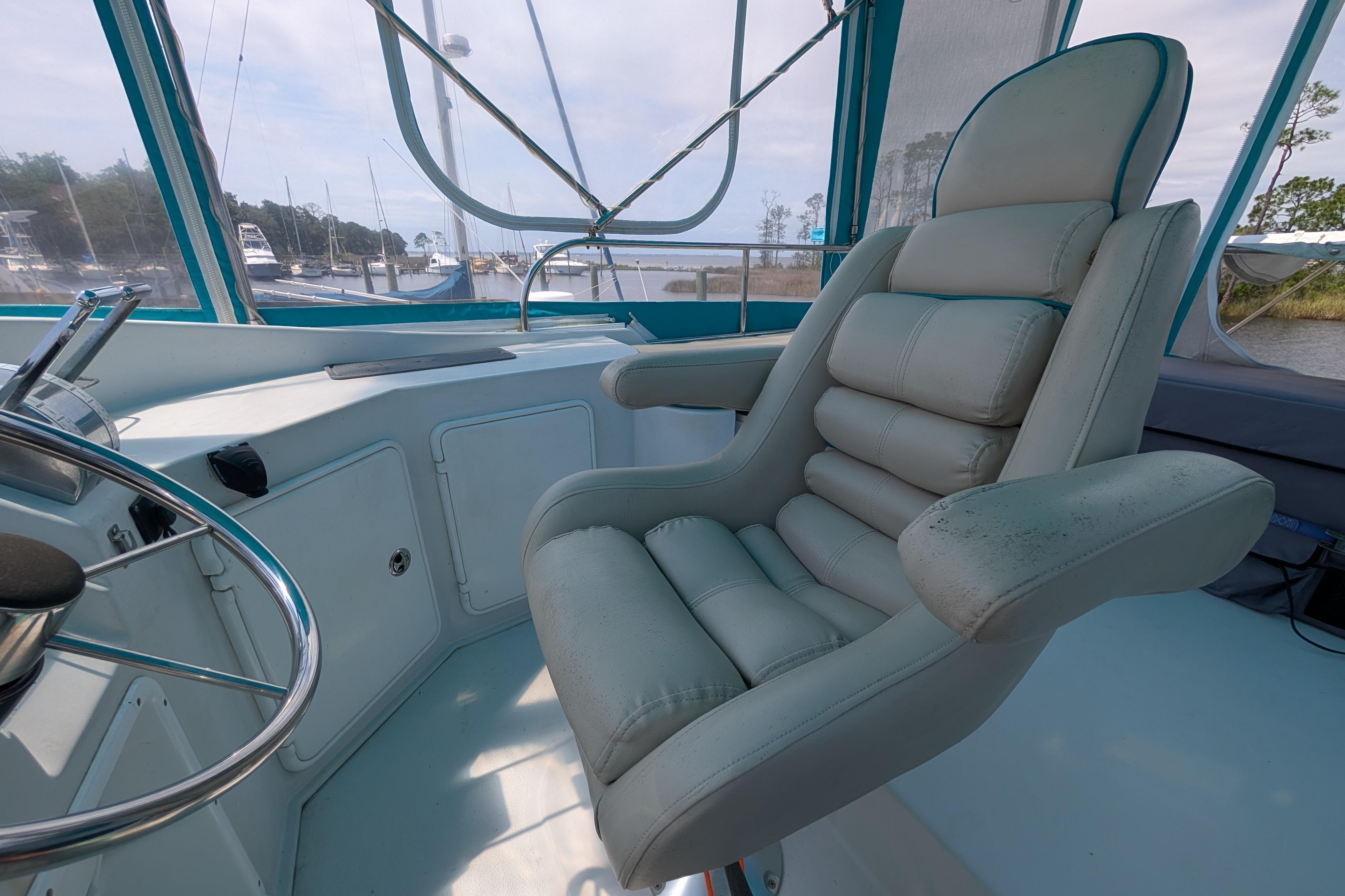 Captain's chair on 2004 PDQ 34 Powercat boat, with steering wheel and marina view.