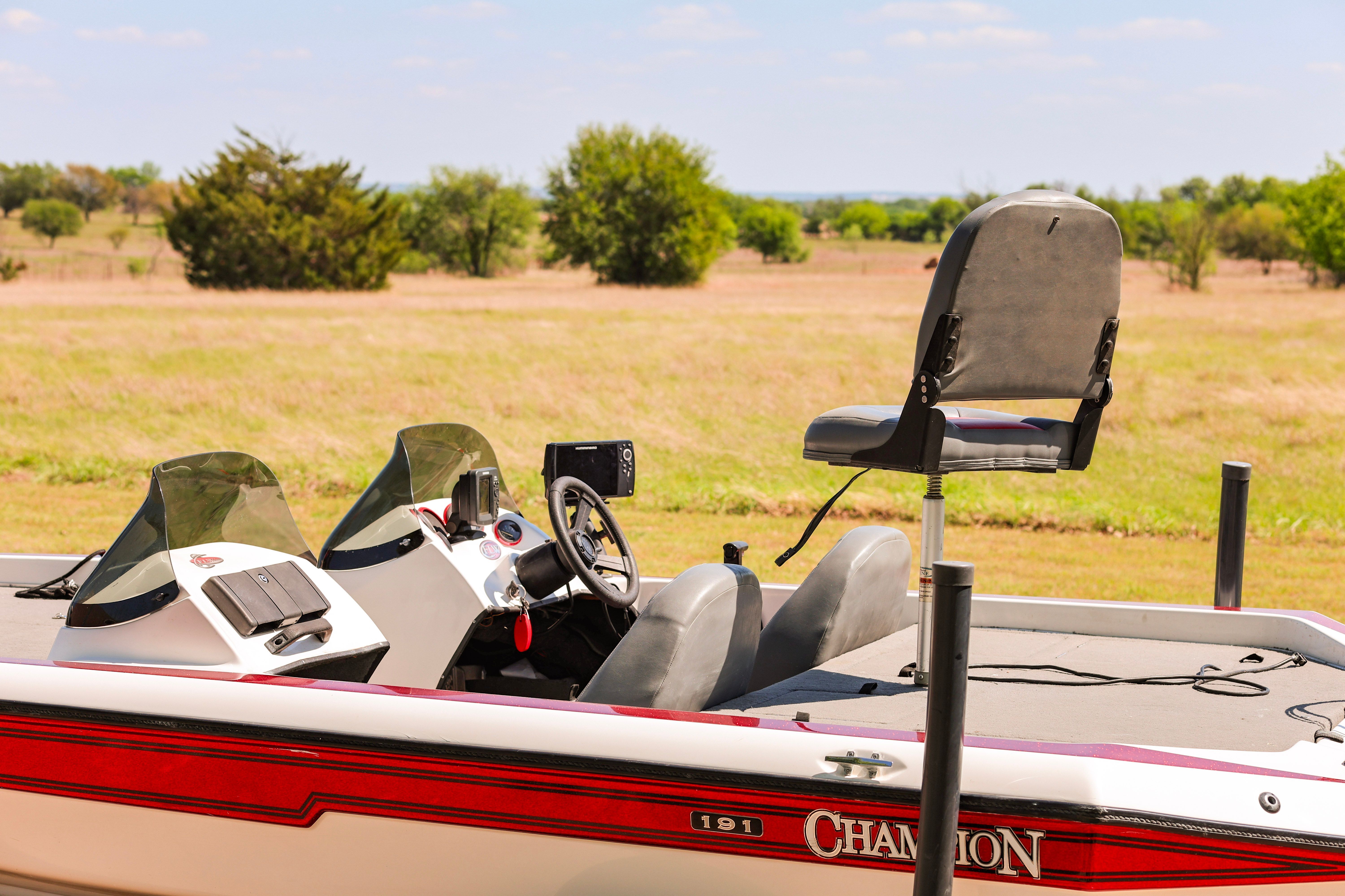A 1999 Champion bass boat is on a field. It features two seats and a steering wheel.