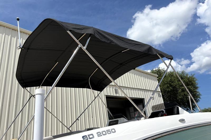 2026 Hurricane SunDeck Sport 2050 OB boat with black canopy, parked outdoors.