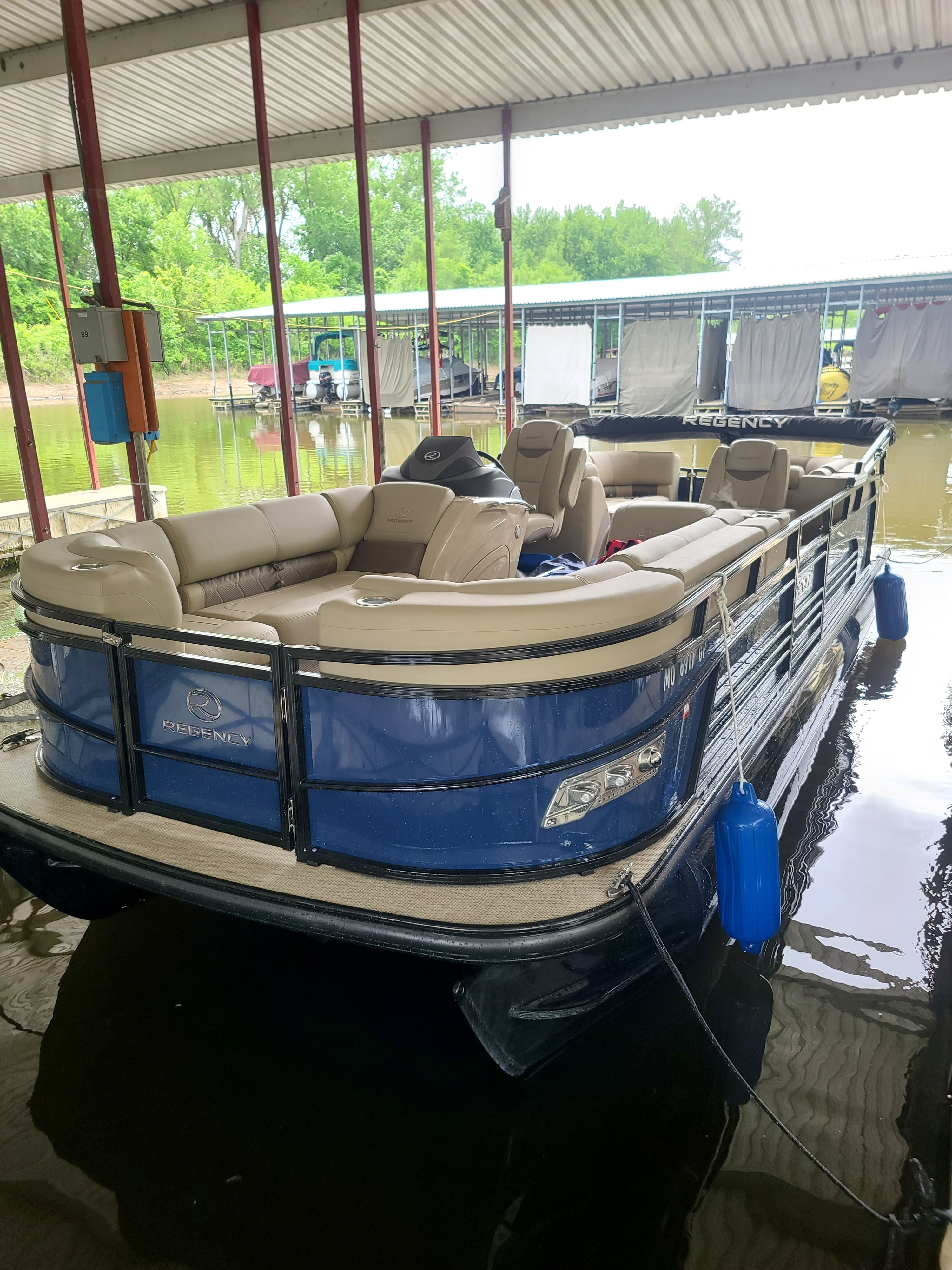 A 2021 Regency 230 LE3 pontoon boat docked under a covered area.