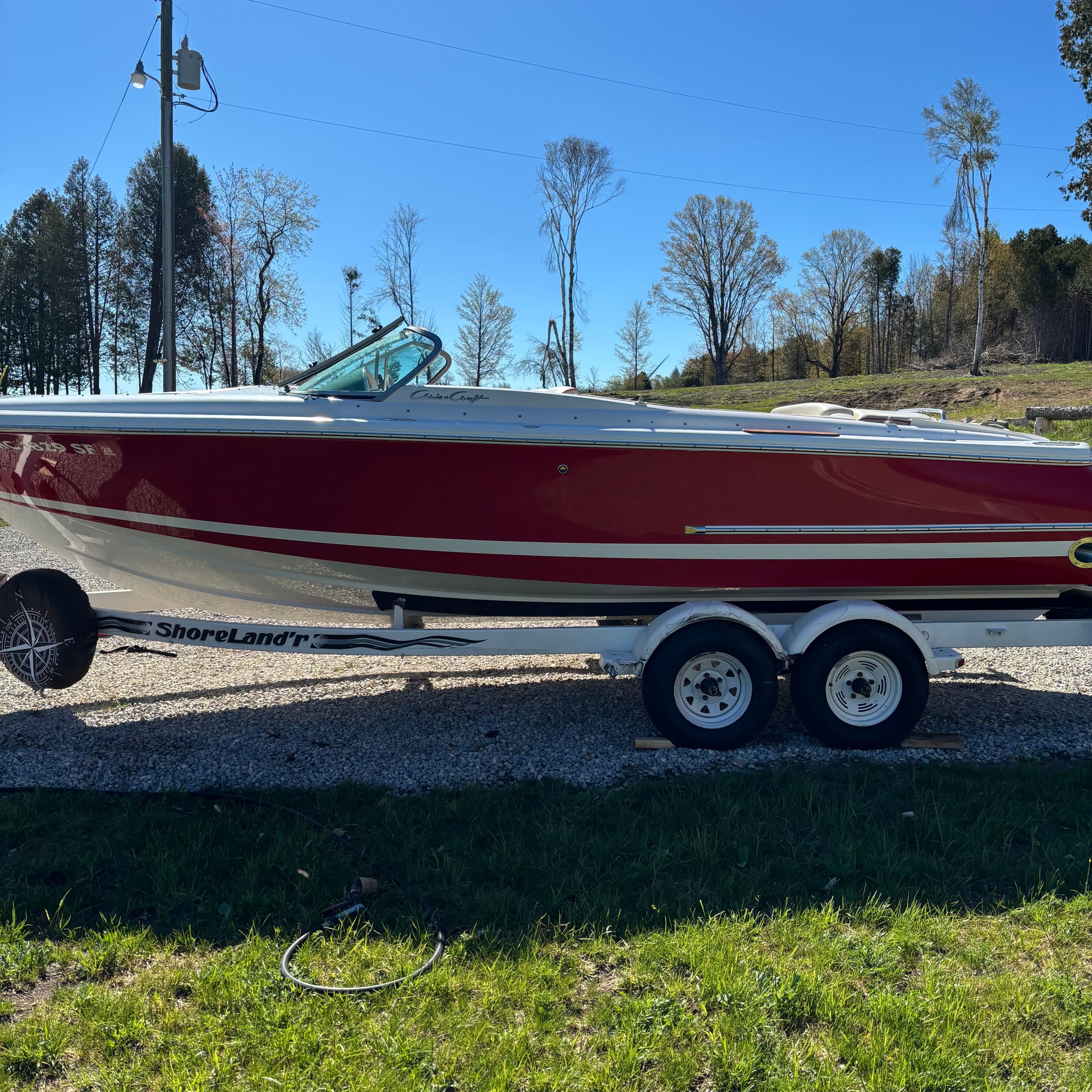 A red 2003 Chris-Craft Launch 22 boat on a trailer on a gravel path.
