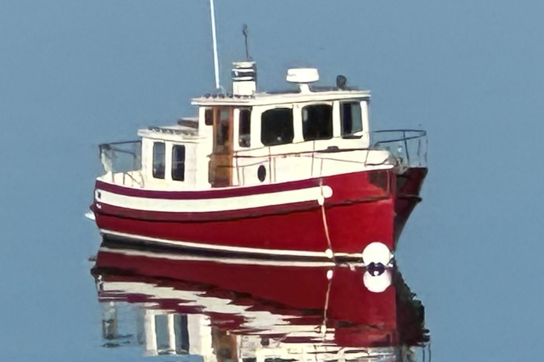 Red 1985 Nordic Tug 26 boat reflecting on calm water.