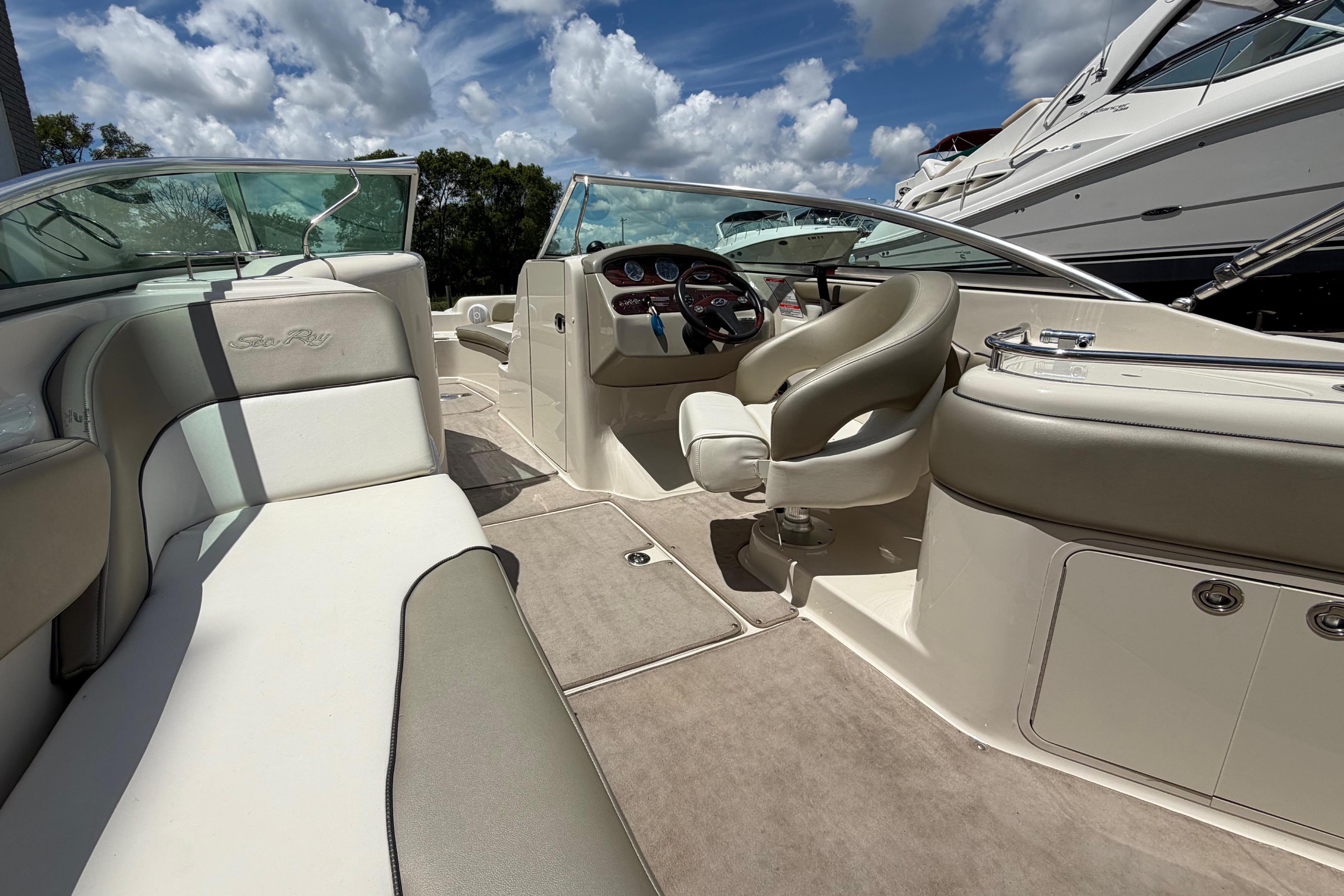 2004 Sea Ray 240 Sundeck interior with beige seating and steering wheel under a blue sky.