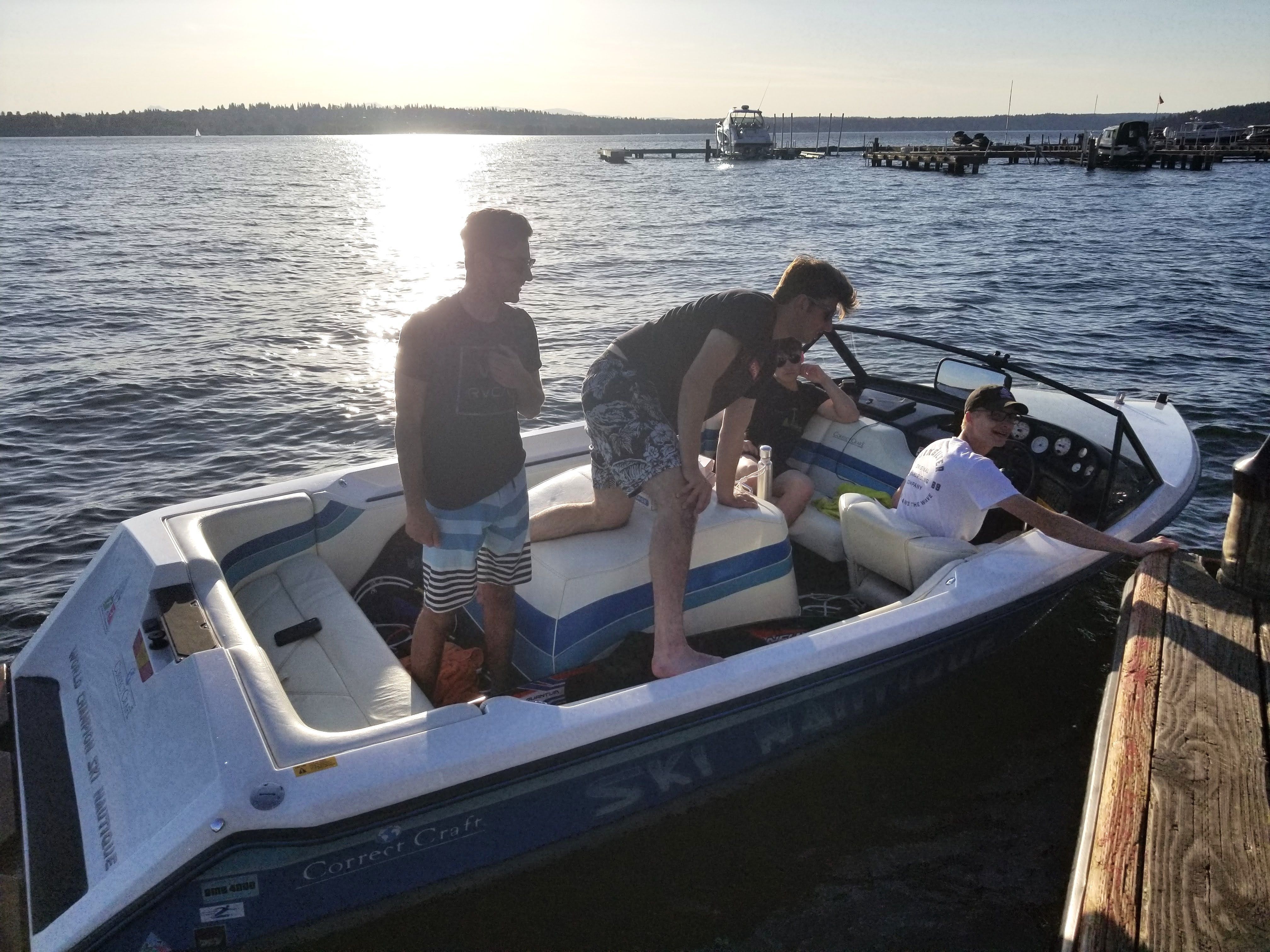 Three people stand on a boat at a dock, surrounded by calm water and a sunny sky.