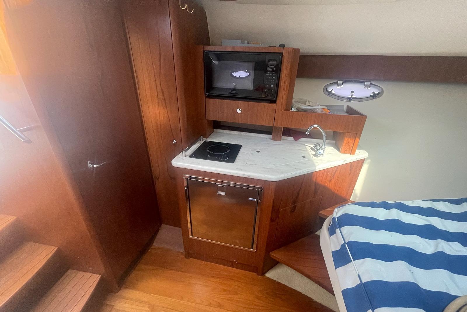 2013 Tiara Yachts 3100 Open cabin with kitchenette and striped bedding.